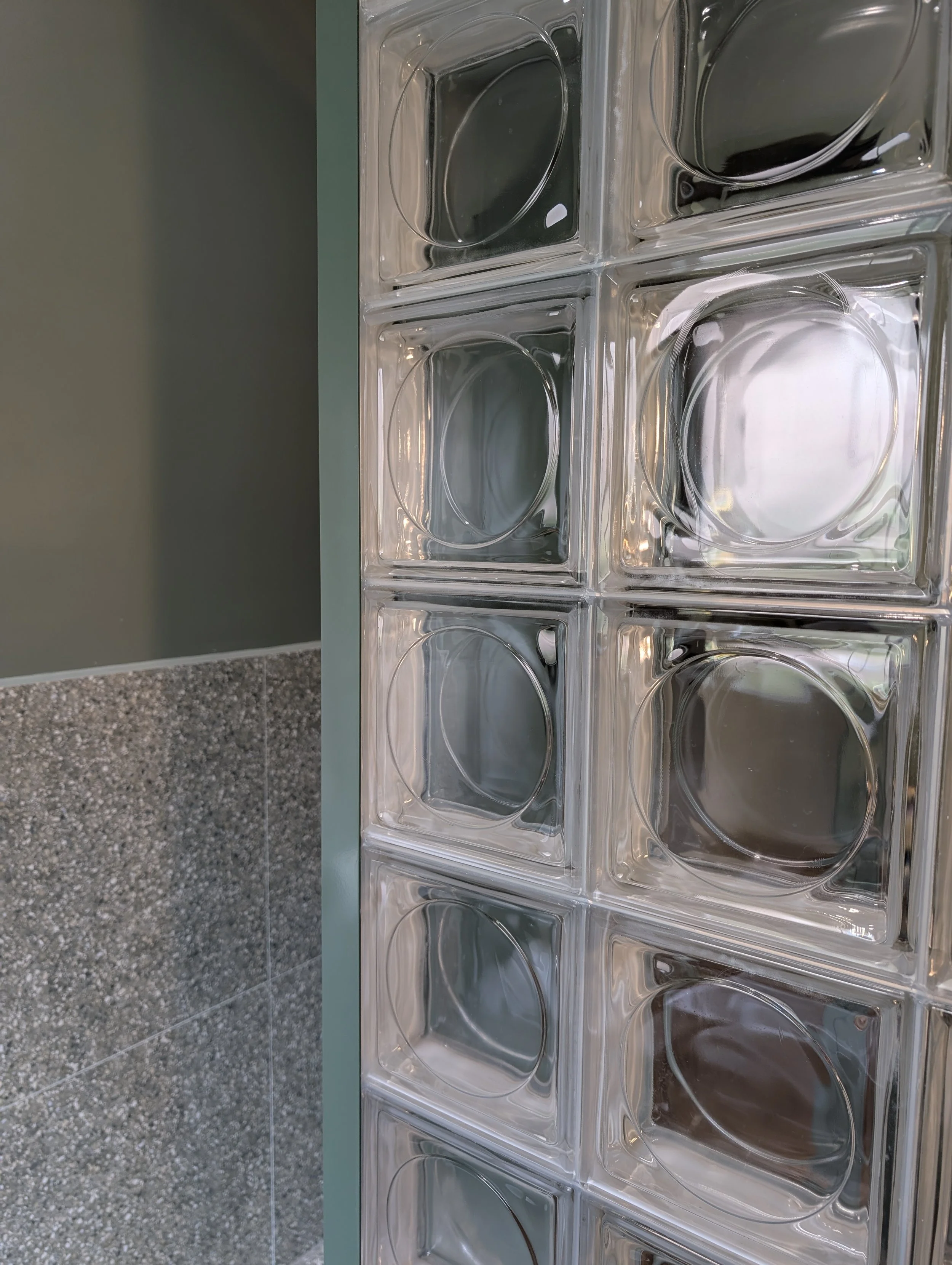 closeup of square glass wall and view of tile and green wall in family bathroom