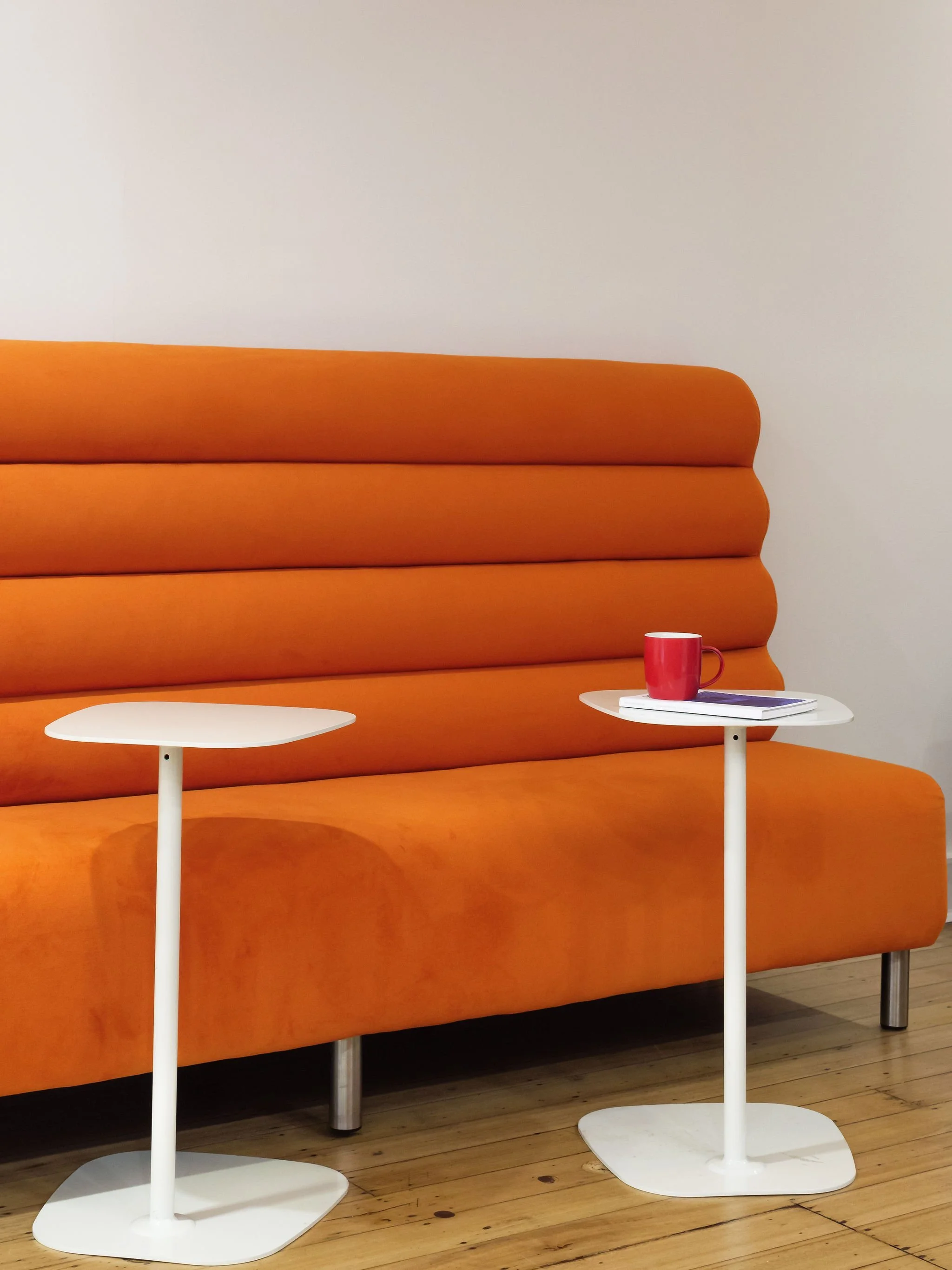 View of the orange couch with modern, white side tables.