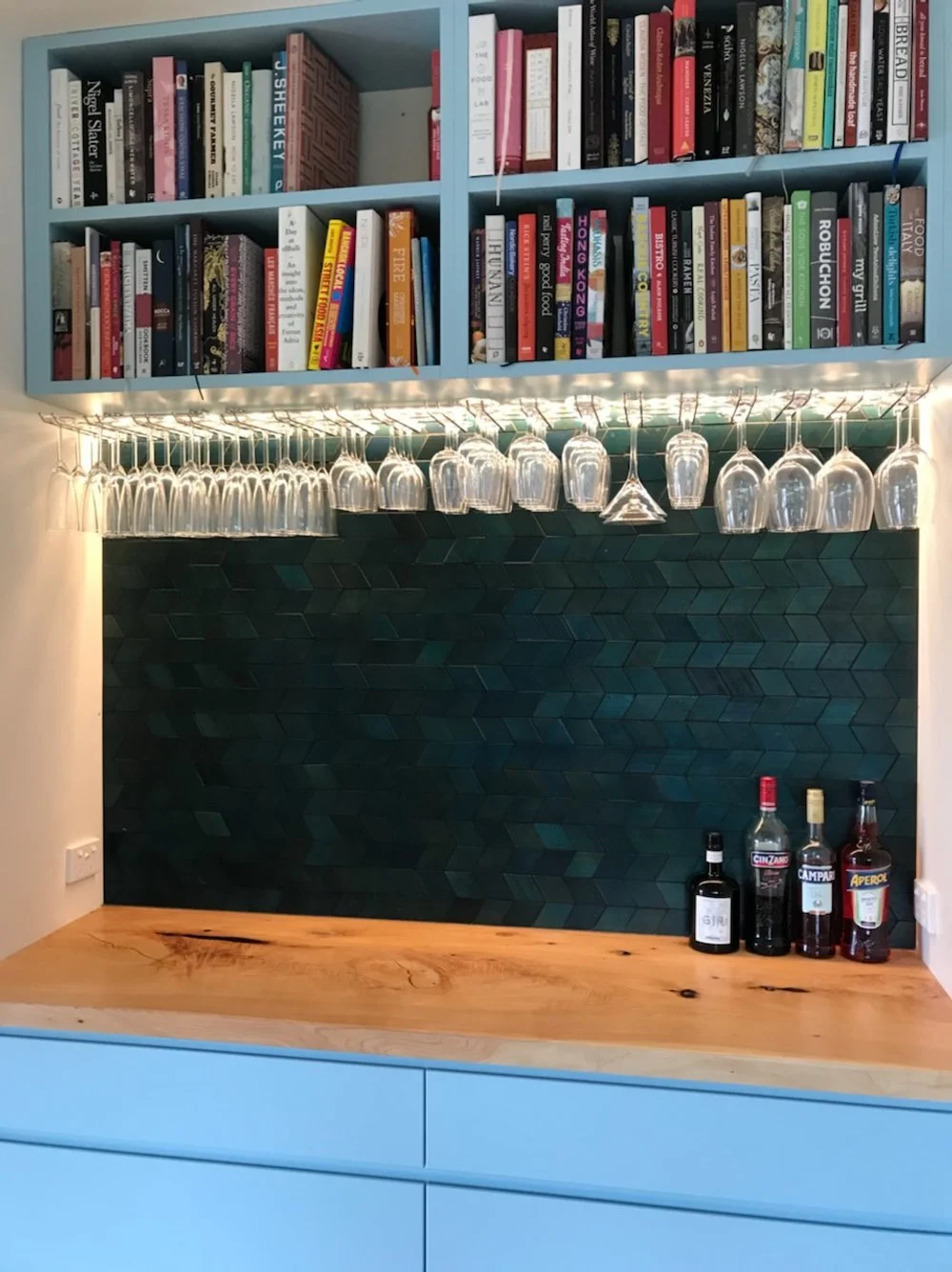 Facing the bar area, showing a rack of glasses, beverage bottles, and a bookshelf above.