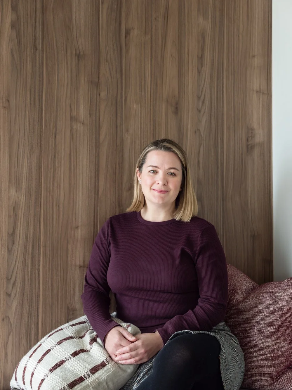Catherine Hamer, interior designer sitting on a couch in front of a wood finished wall