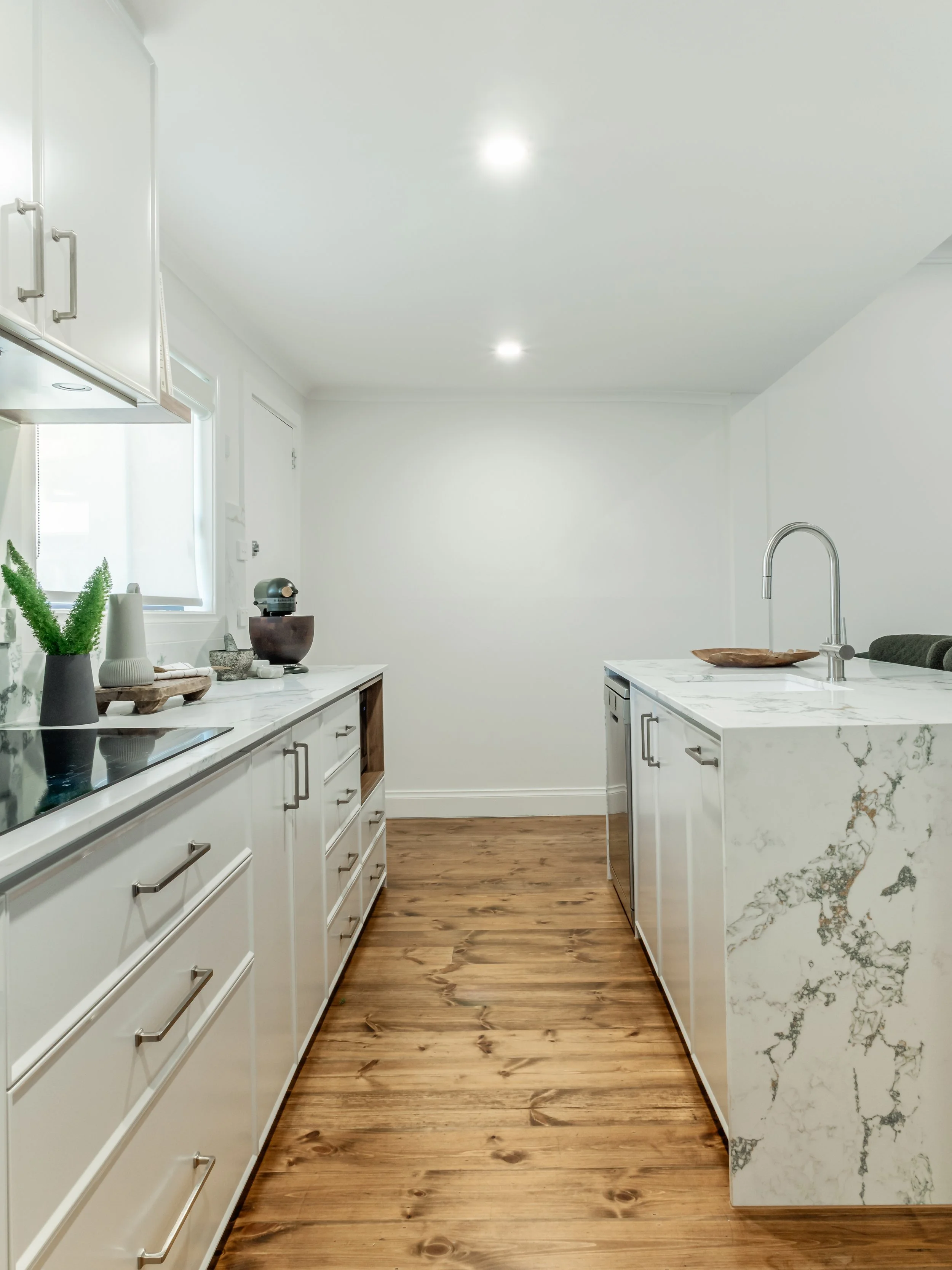 wide view of kitchen preparation area, with white walls, stone benches, wooden floor. contemporary feel 