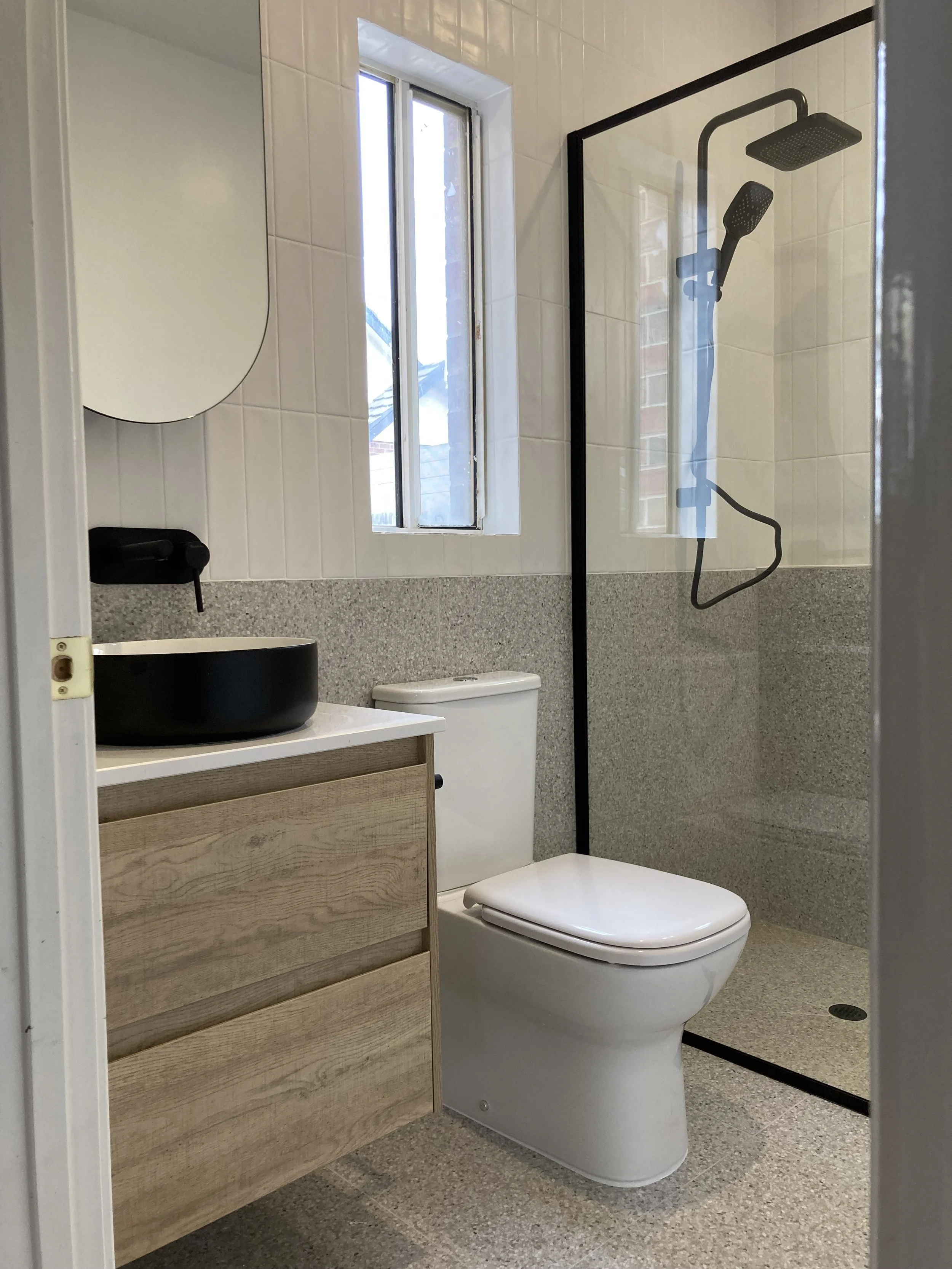 Complete redesign of laundry to bathroom, with contemporary design and refined material selection. We can see wooden cabinets, modern and minimal basin, toilet, and shower.