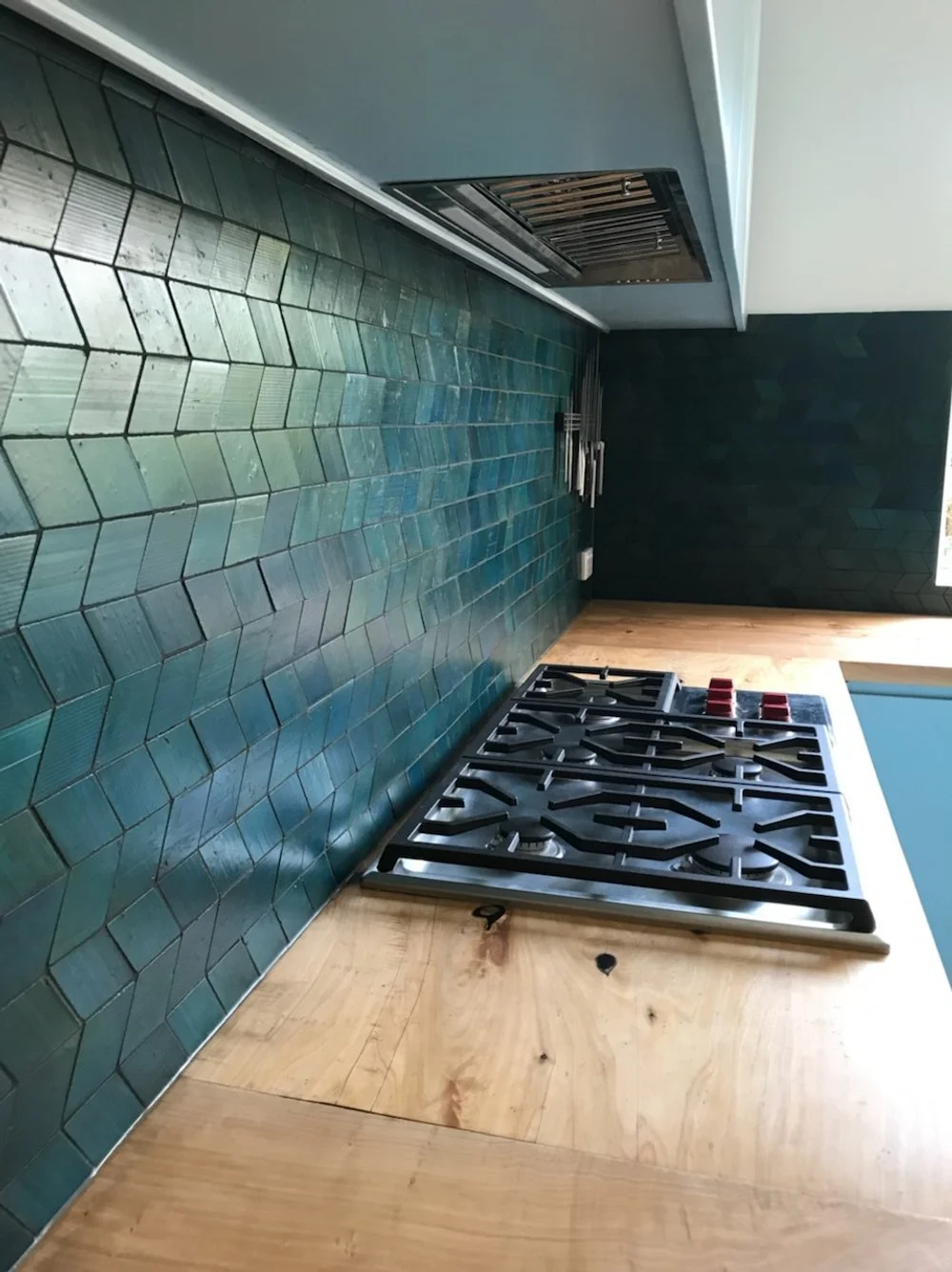 Elegant green tiles, balance against the light wood countertop, and gas stovetop.