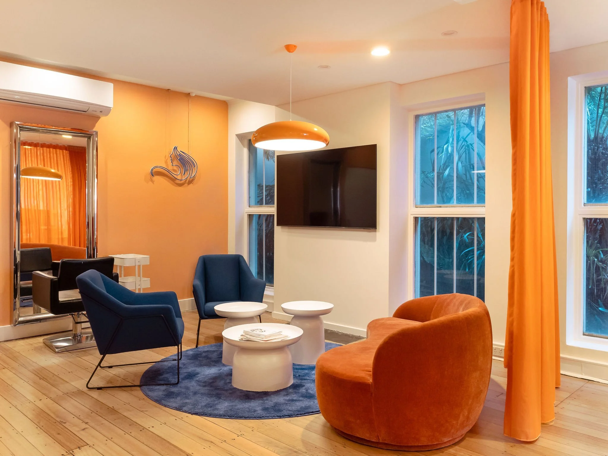 Open plan sitting area, featuring modern interior design choices to reflect brand identity, blues and oranges. Repurposed hair salon objects in background.