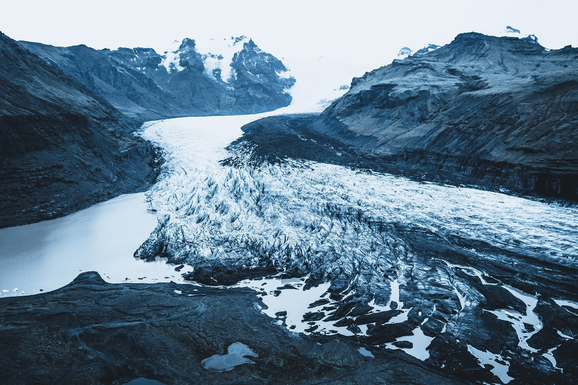 Gletscher in einer Bergregion mit schneebedeckten Gipfeln im Hintergrund und fließendem Eis und Wasser im Vordergrund.