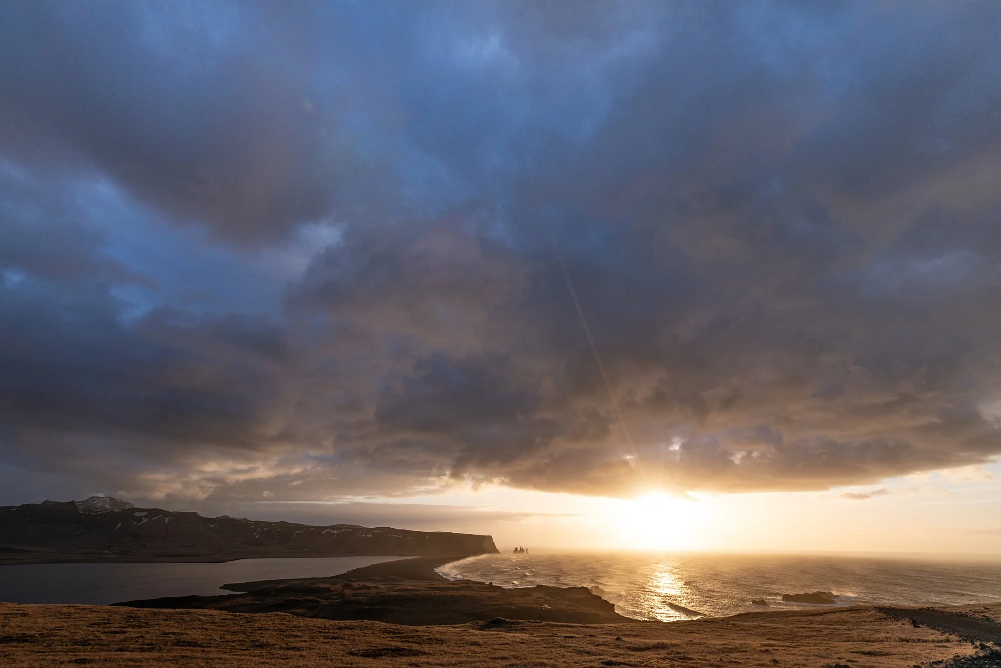 Landschaft am Meer bei Sonnenuntergang mit dunklen Wolken am Himmel.