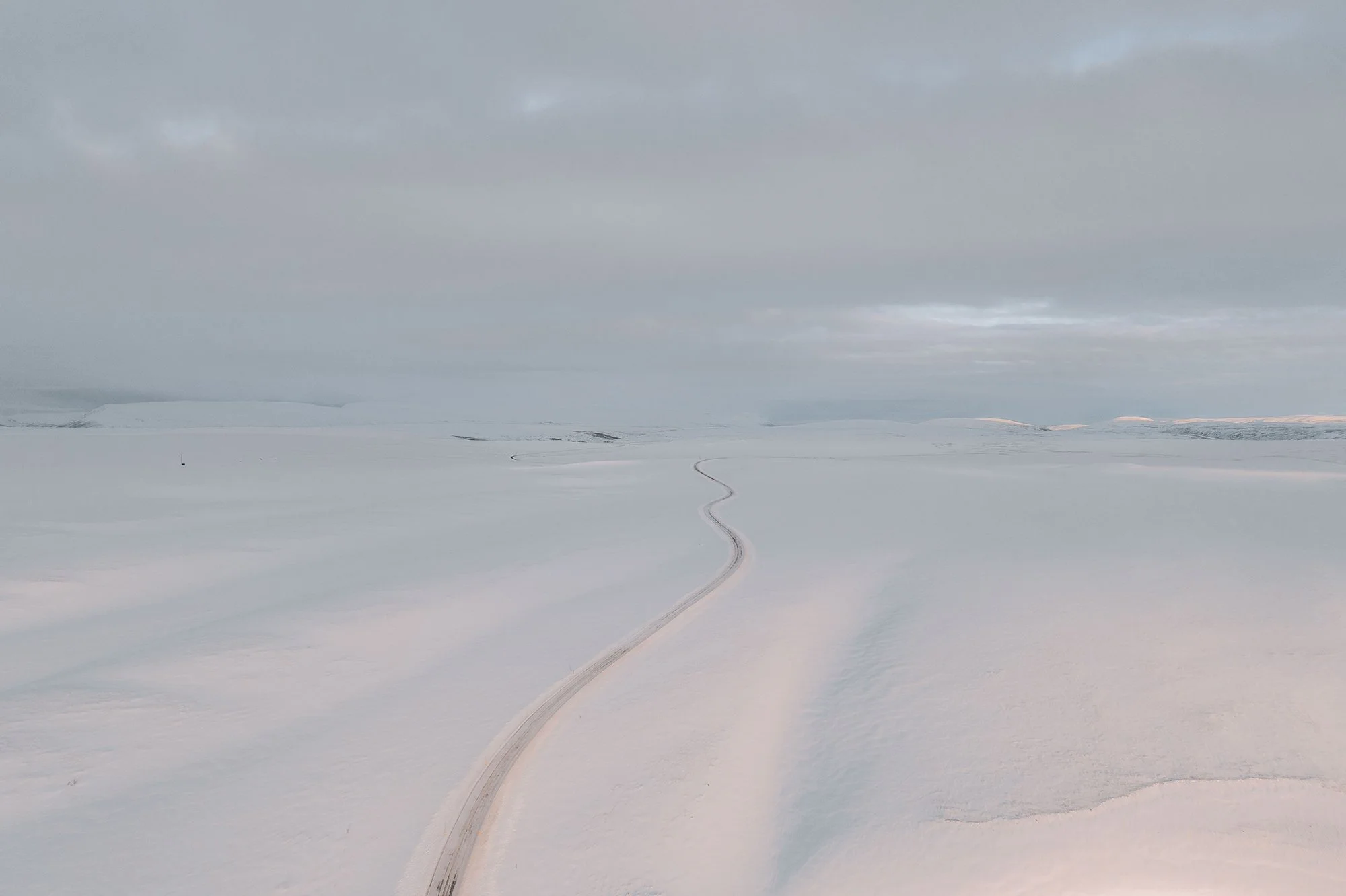 Schneebedehnte Landschaft mit einer kurvigen Schneepiste und bewölktem Himmel, keine sichtbaren Menschen oder Tiere.