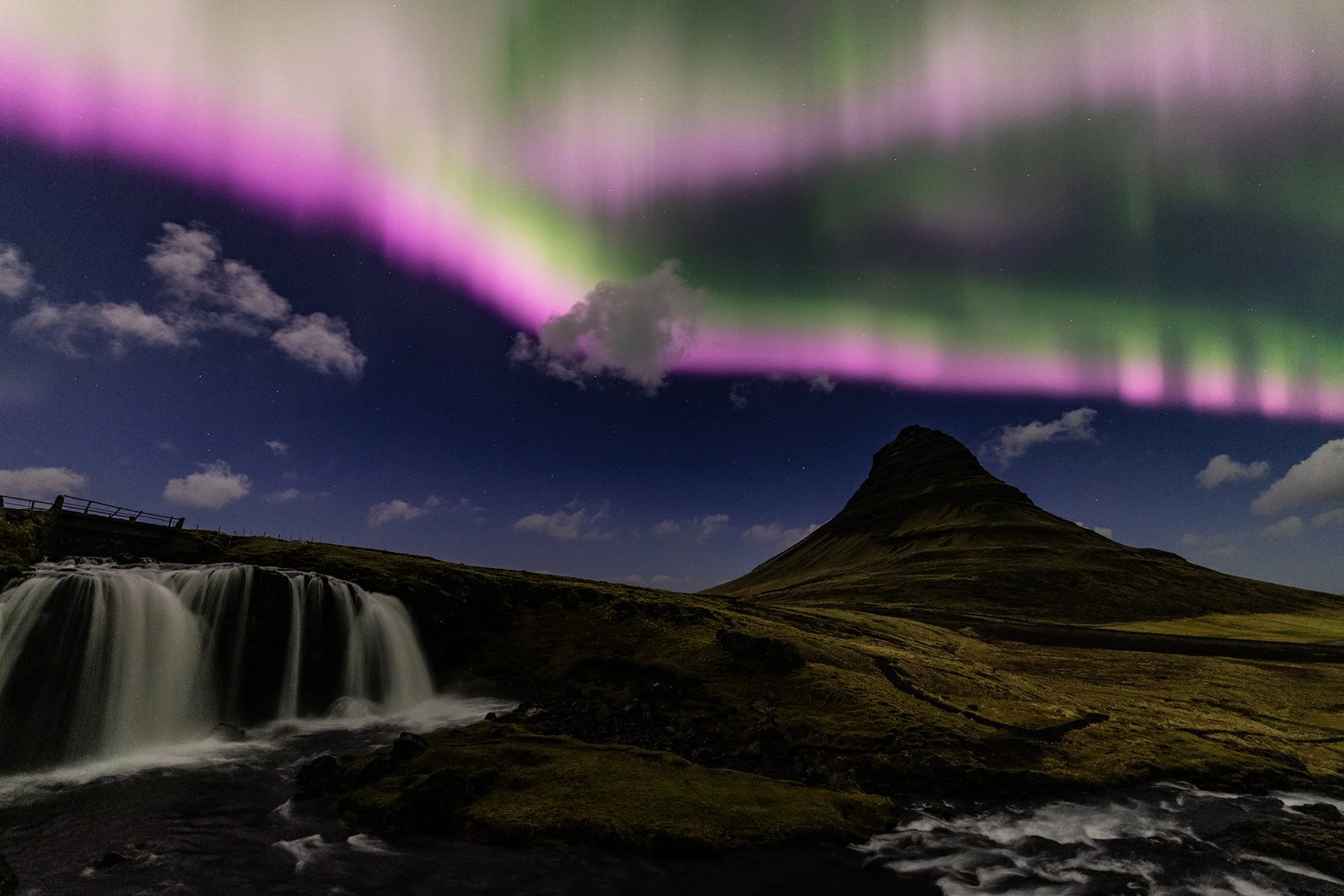 Nordlichter über lavaförmigem Berg mit Wasserfall im Vordergrund bei Nacht.