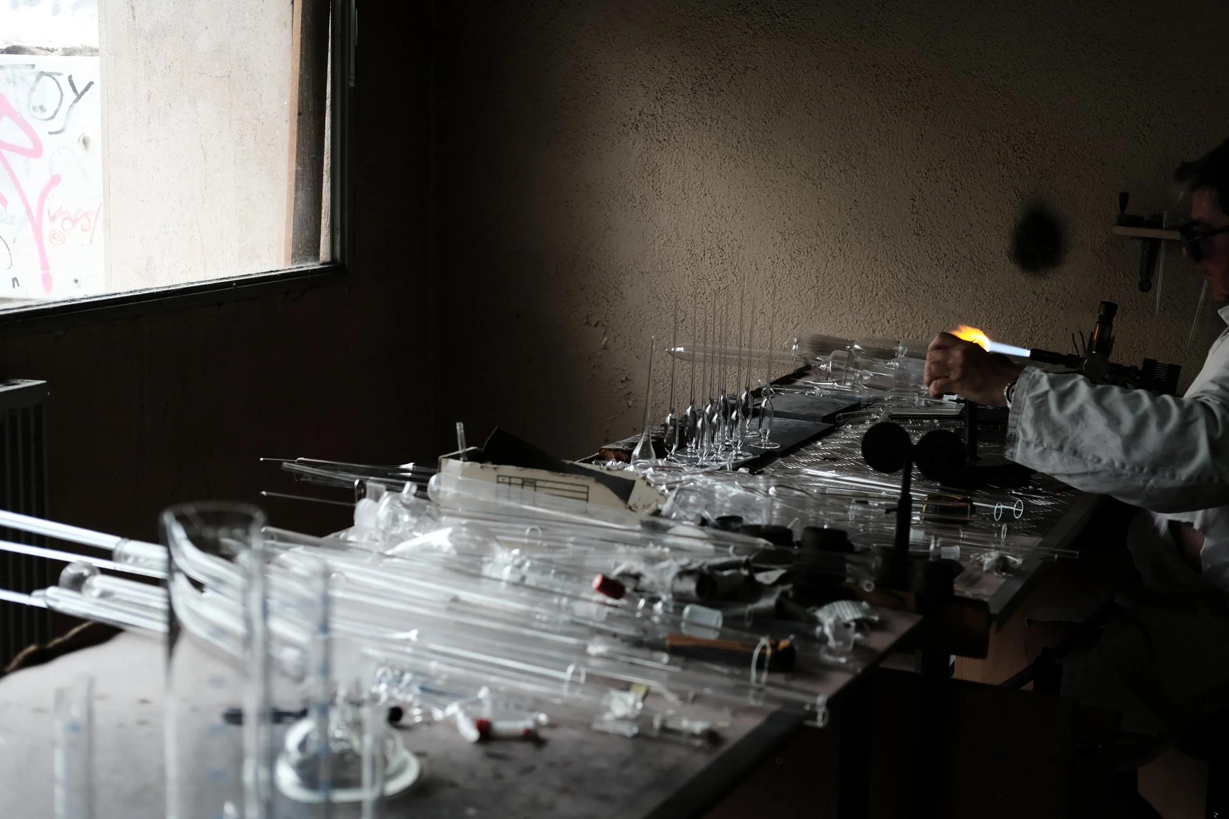 Un laboratoire sombre avec une personne en protecteur blanc utilisant un tube à essence, entouré de nombreux tubes en verre sur une table.