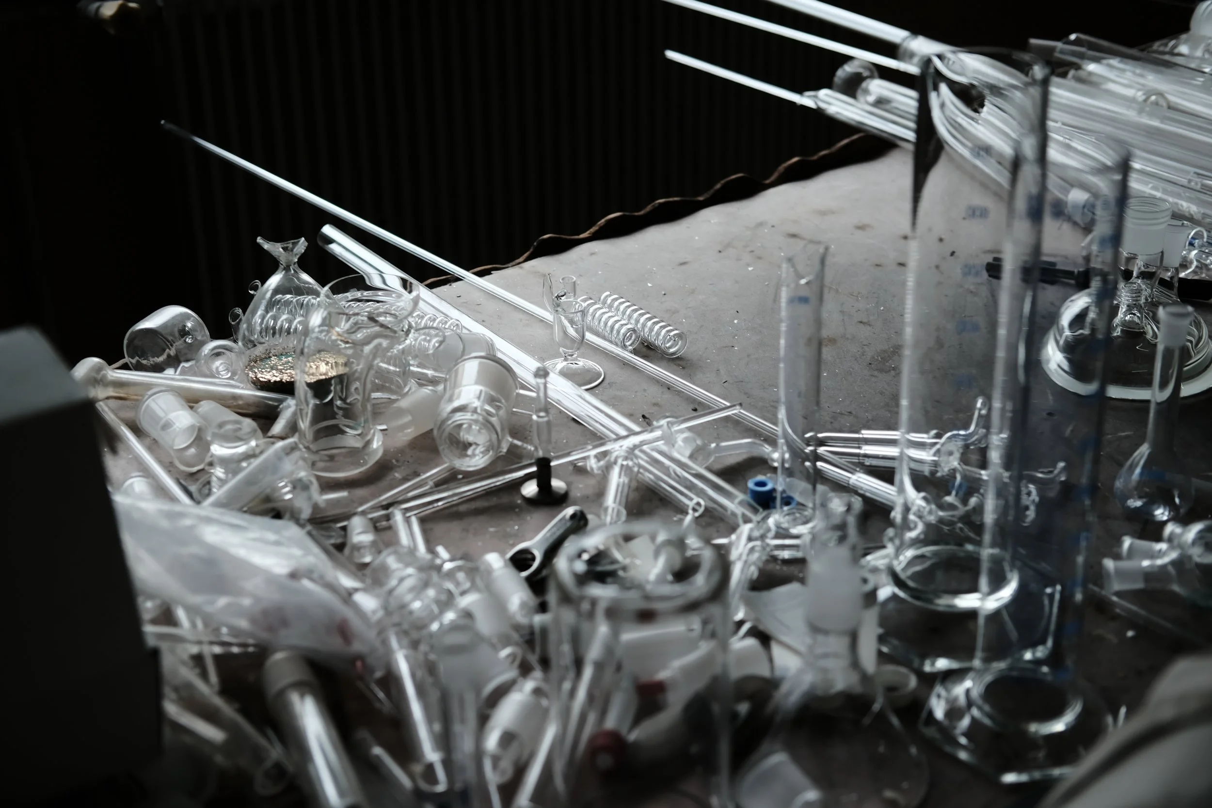 Un tas de tubes en verre et d'objets de laboratoire cassés ou abandonnés sur une surface, dans un environnement sombre. 