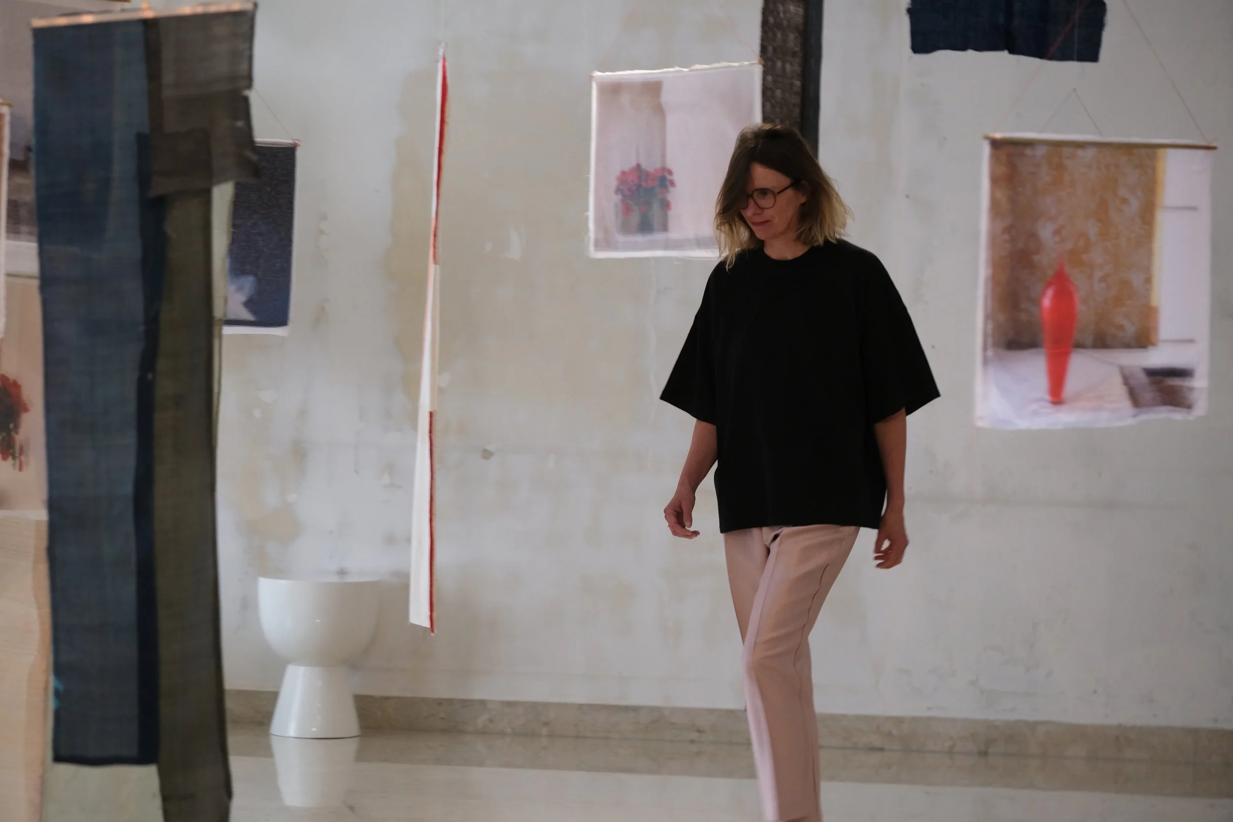 Femme marchant dans un musée ou une galerie, vue à travers une vitre ou un miroir, avec des œuvres d'art suspendues au mur.