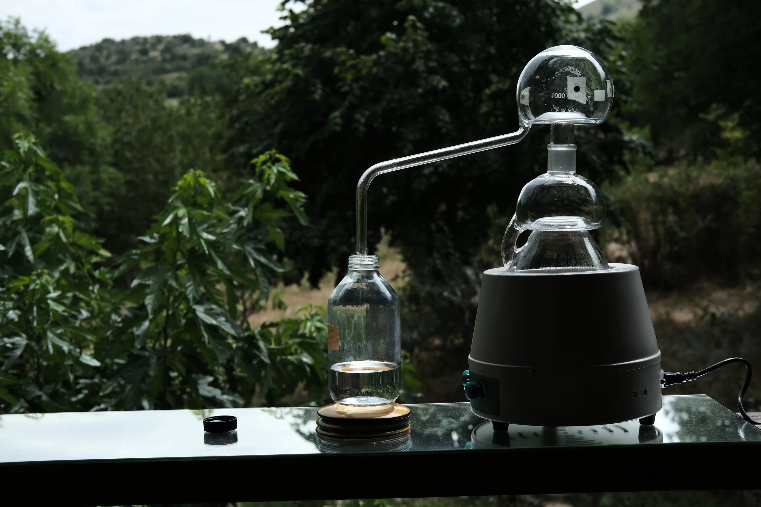 Un dispositif de laboratoire en verre utilisé pour réaliser une expérience est placé à l'extérieur, probablement en raison de la nature de l'expérience, avec un décor de nature en arrière-plan.