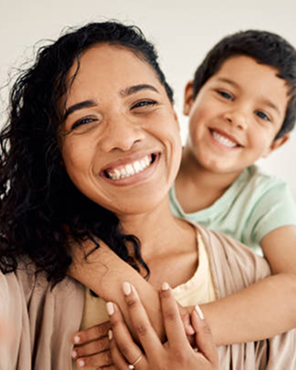 Woman smiling with child on her back, both showing joyful expressions.