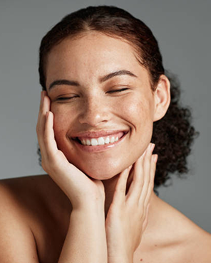 Woman smiling with closed eyes, hands on face, neutral background