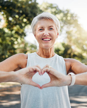 Elderly woman smiling outdoors, making a heart shape with hands