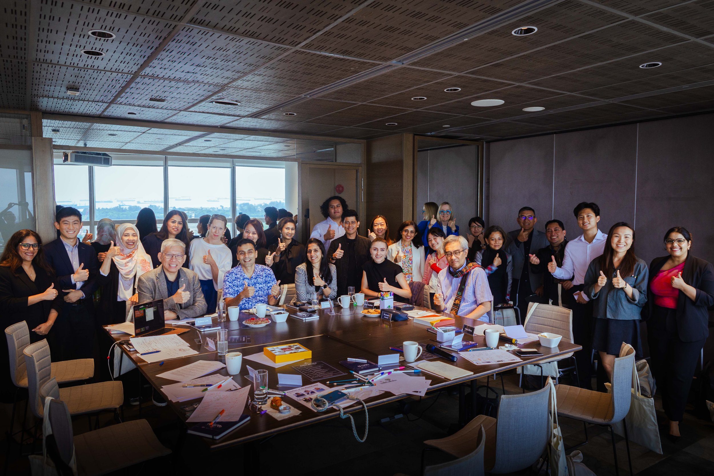 Group of diverse professionals gathered in conference room, smiling and giving thumbs up.