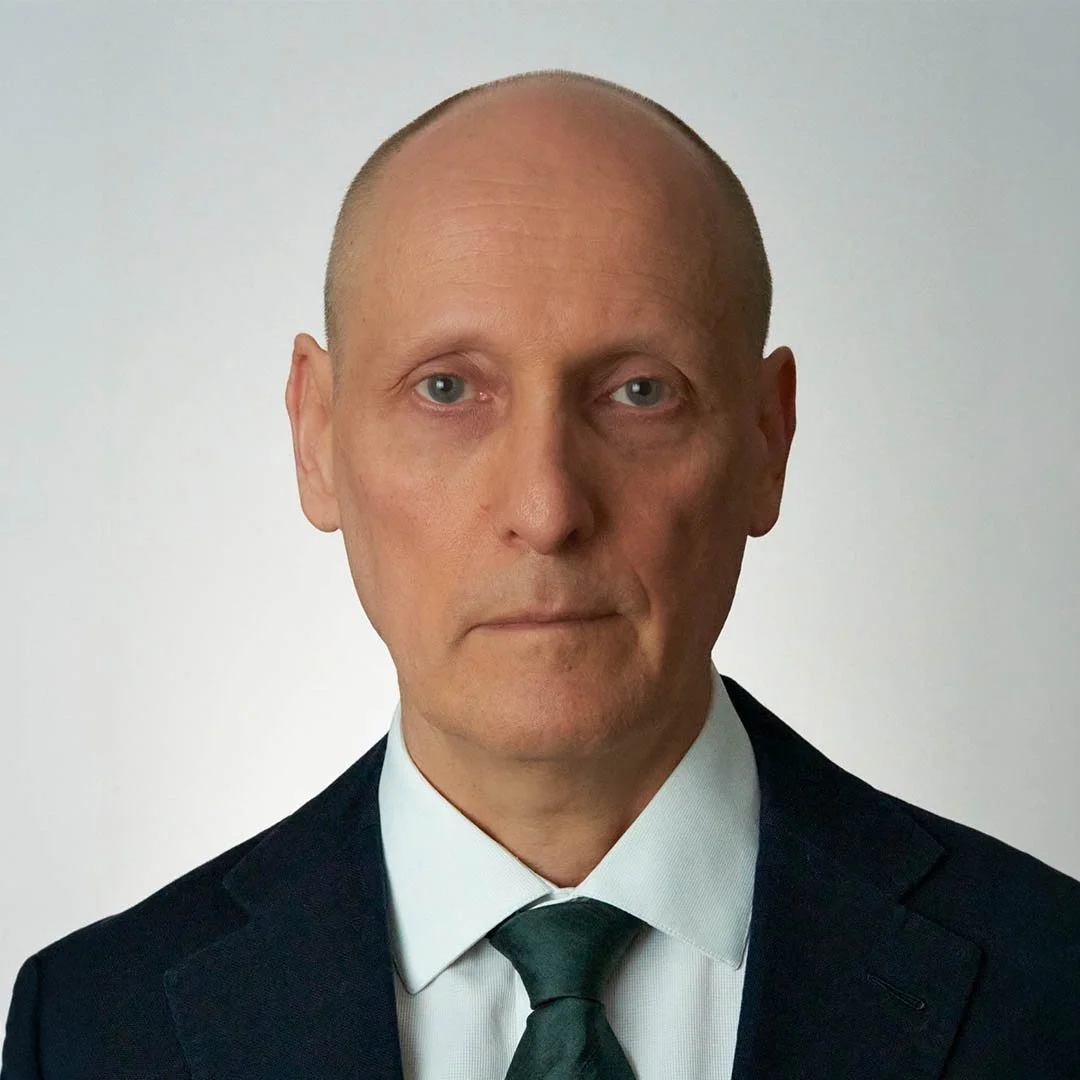 A portrait of a middle-aged man with a serious expression, wearing a dark suit, white shirt, and a dark green tie, against a plain light background.