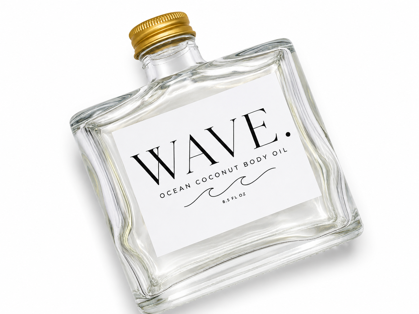 A clear glass bottle of WAVE ocean coconut body oil with a gold cap, lying on a white surface.
