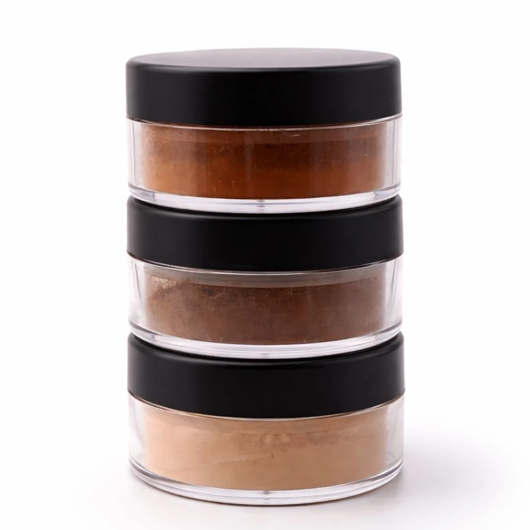 Stack of three round containers with black lids, filled with different shades of brown powder, on a white background.