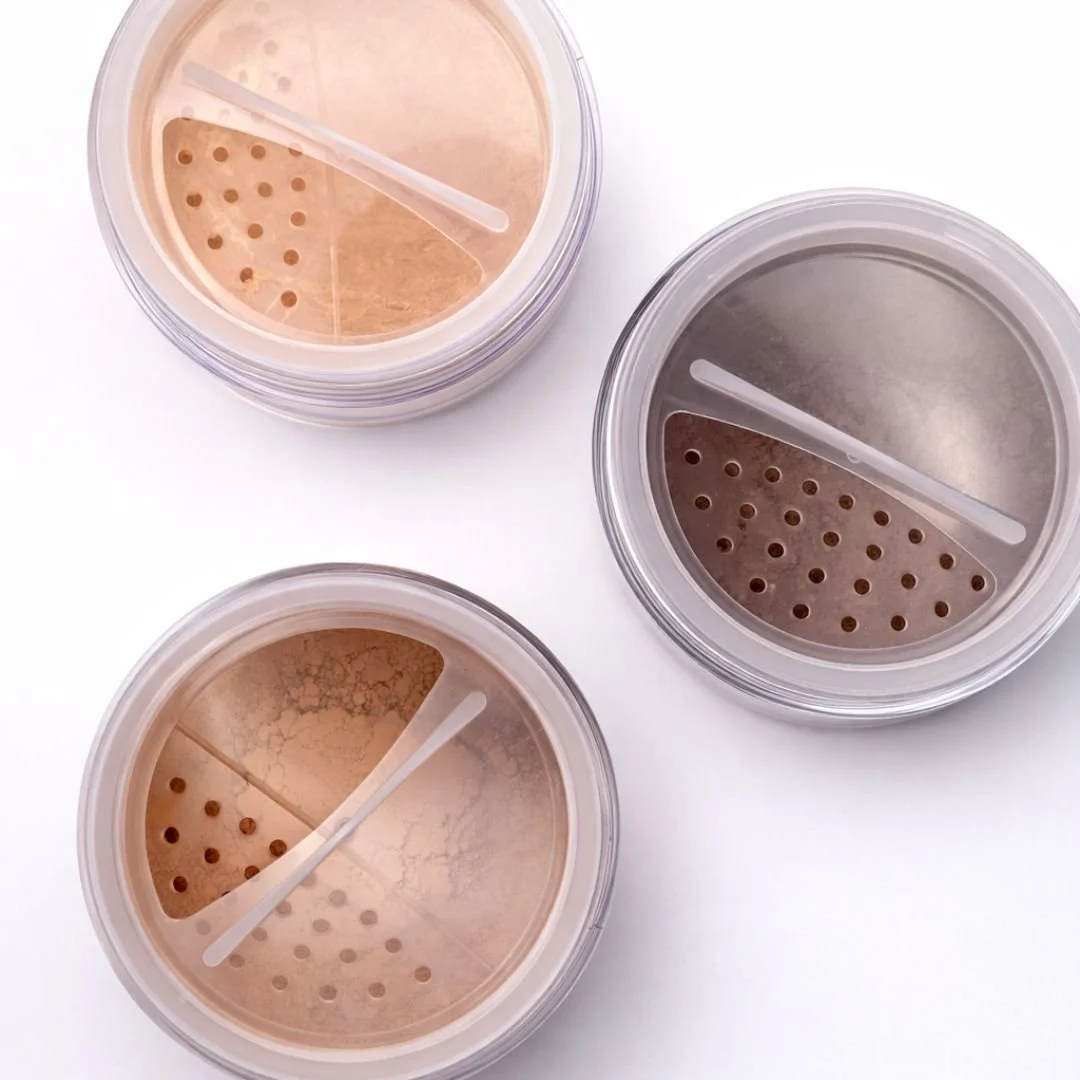 Three plastic containers of loose face powder with sifter lids, each divided into light and dark shades, on a white surface.