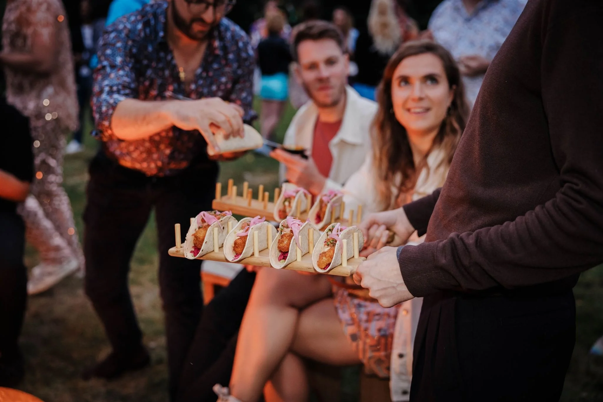 People at an outdoor gathering holding trays of tacos.