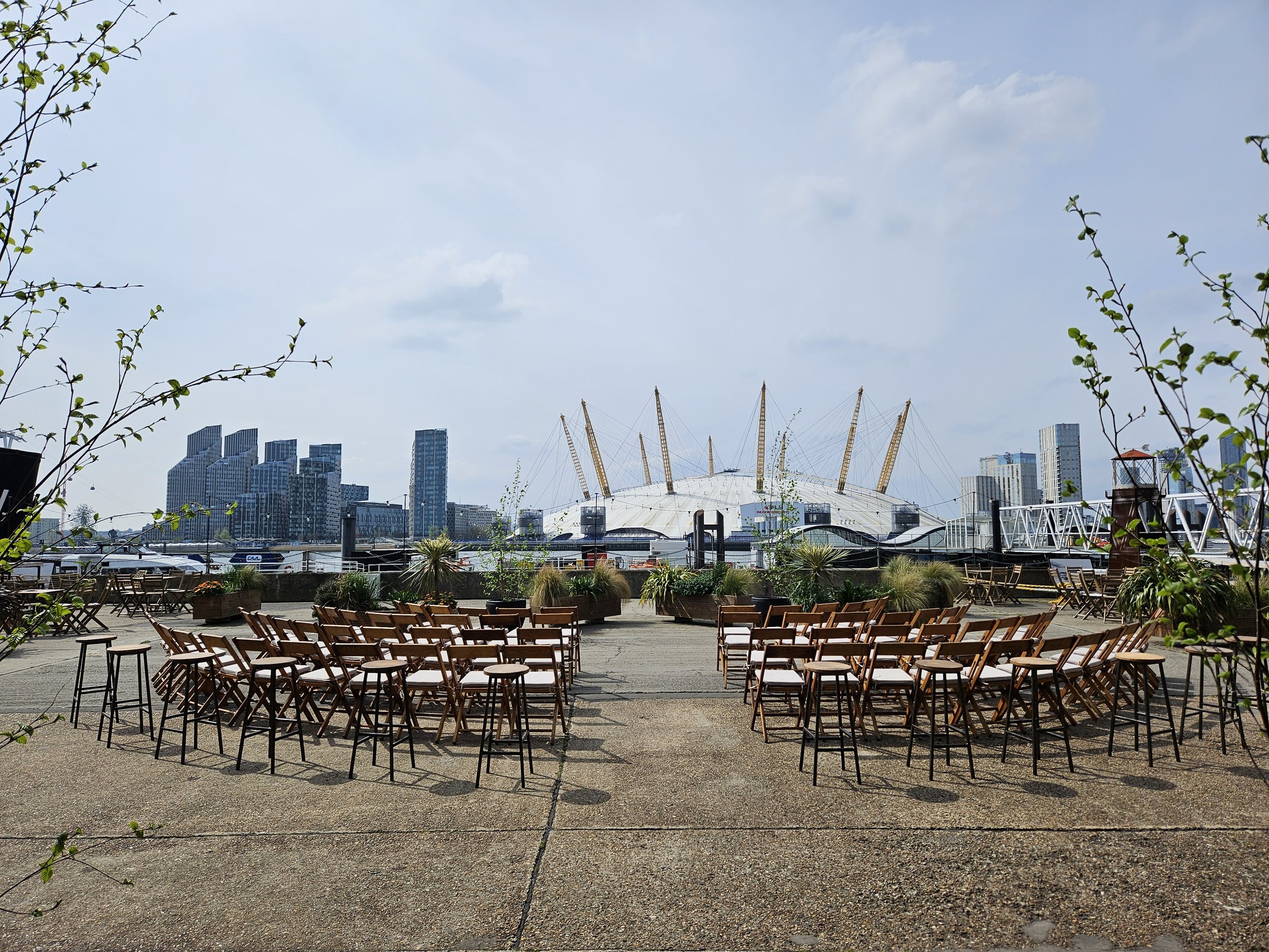 Outdoor seating area on a courtyard with wooden chairs and tables, plants, and London skyline.