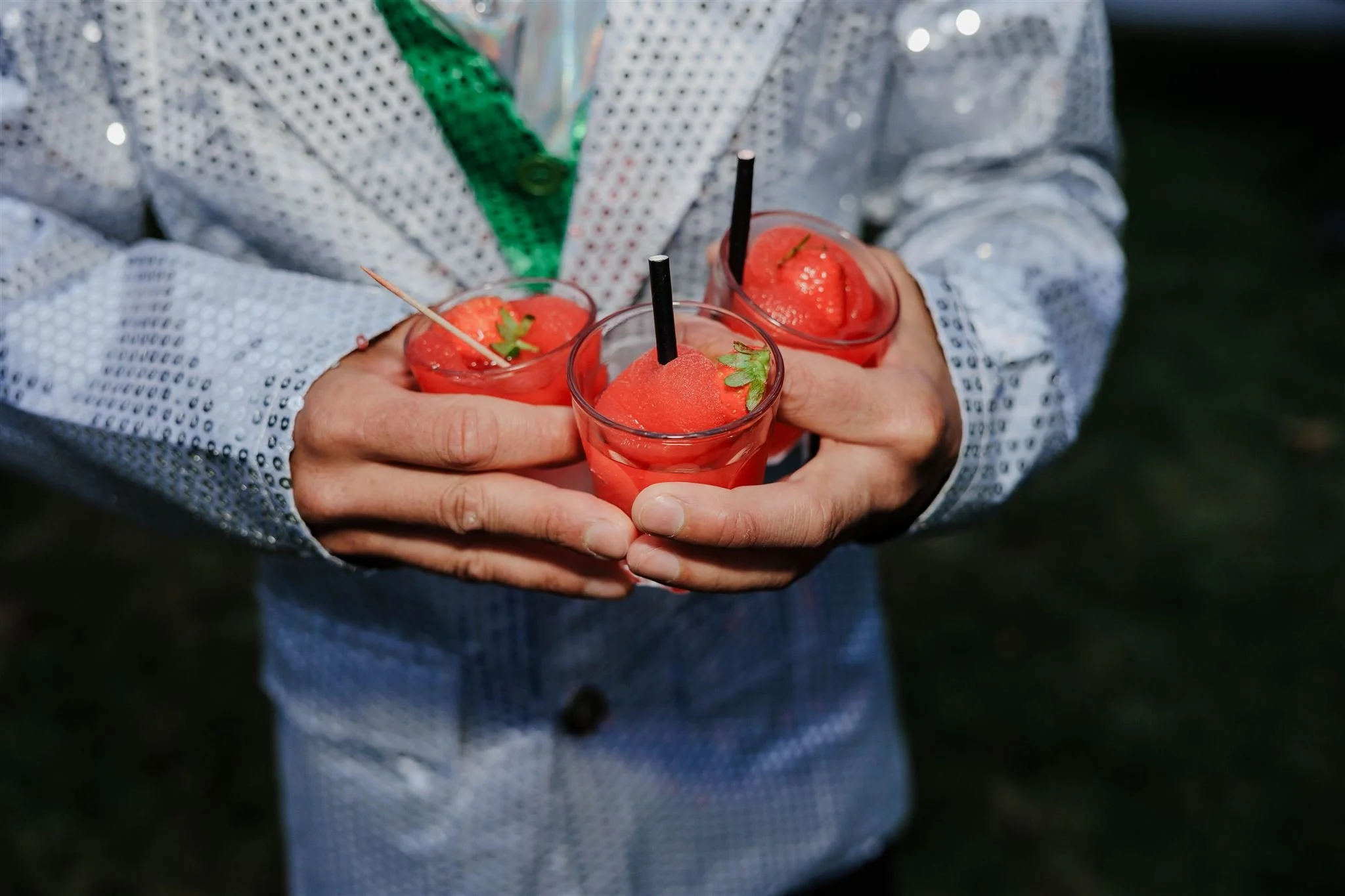 Person holding three drinks with strawberries and garnishes in clear glasses.