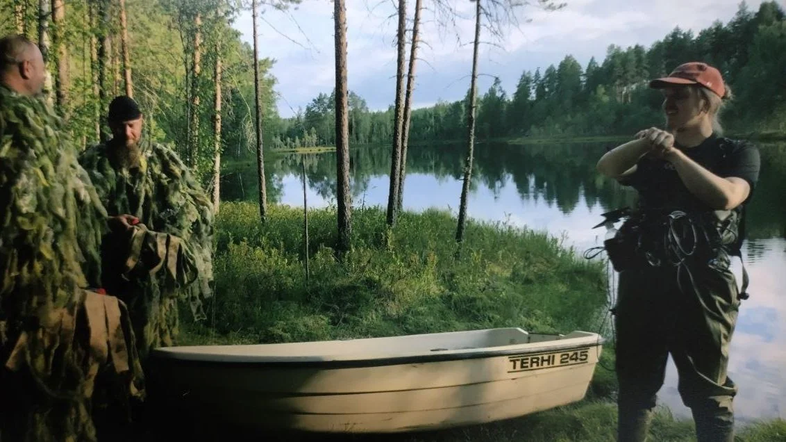 Three people preparing for a water activity near a lake, with a boat on the shore and surrounded by trees. Memories Move Like Distant Island - BTS Wet recording prep