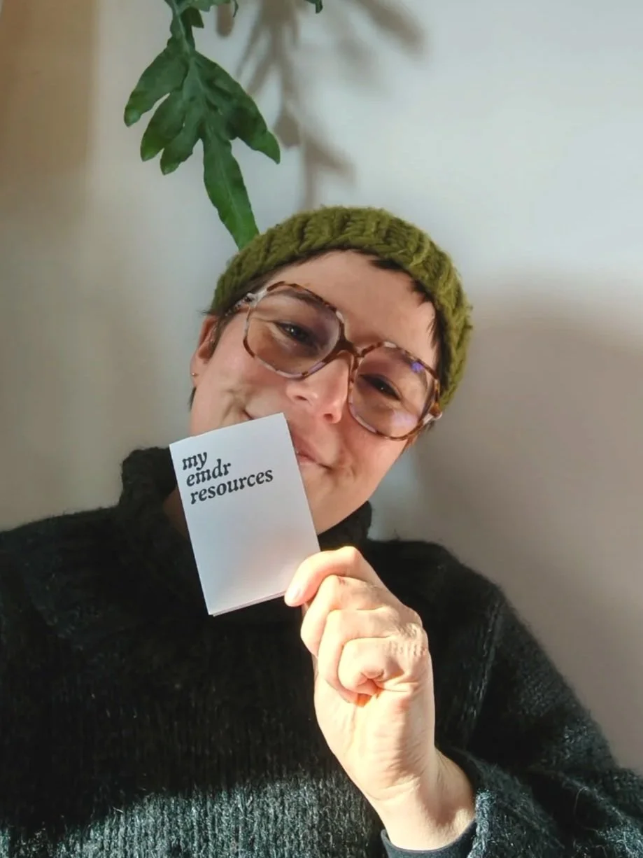 Rhiannon, a white person in a green beanie and big glasses, holds a mini-zine. The cover says "my emdr resources"