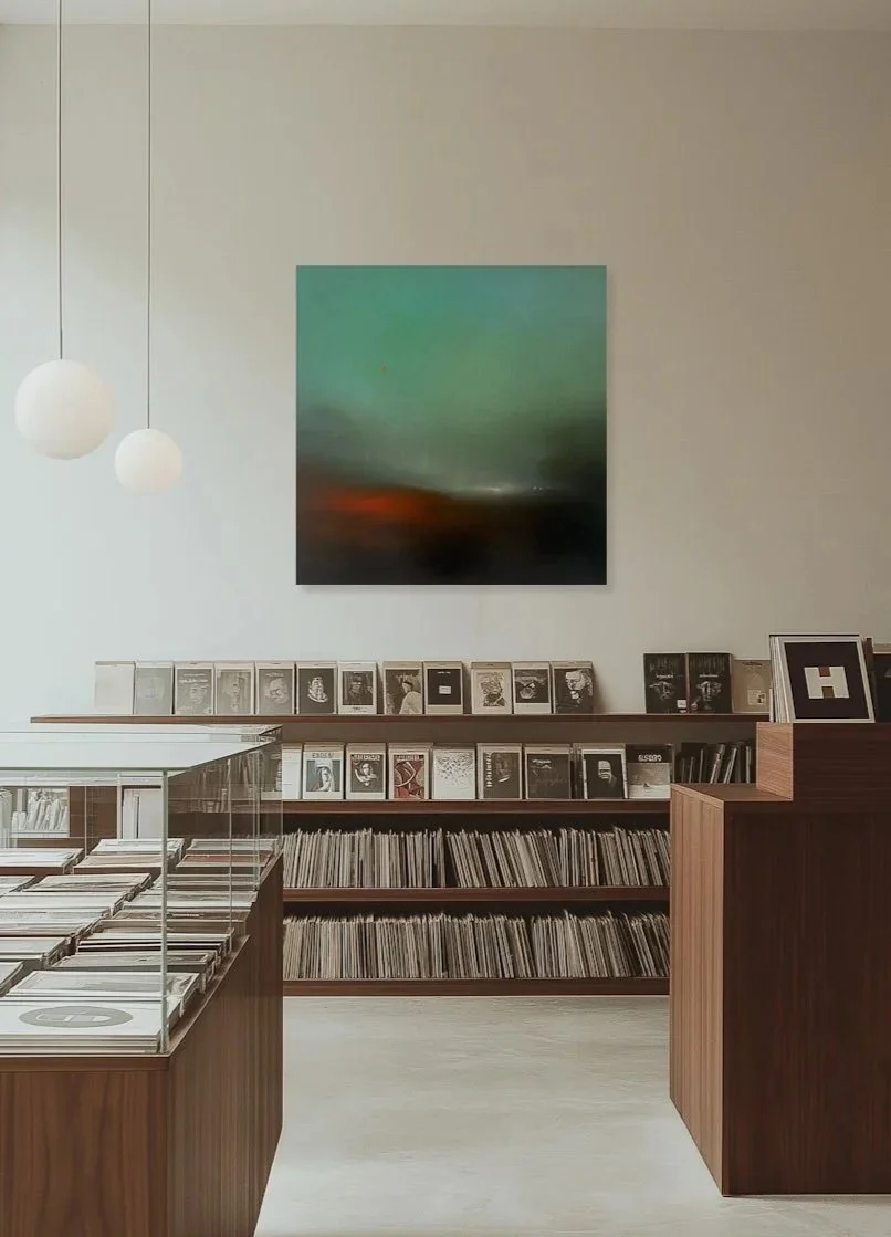 Intérieur d'une librairie ou d'un magasin de disques avec des étagères remplies de livres ou de vinyles, une peinture abstraite au mur, deux lampes suspendues rondes et une vitrine en verre contenant des disques.