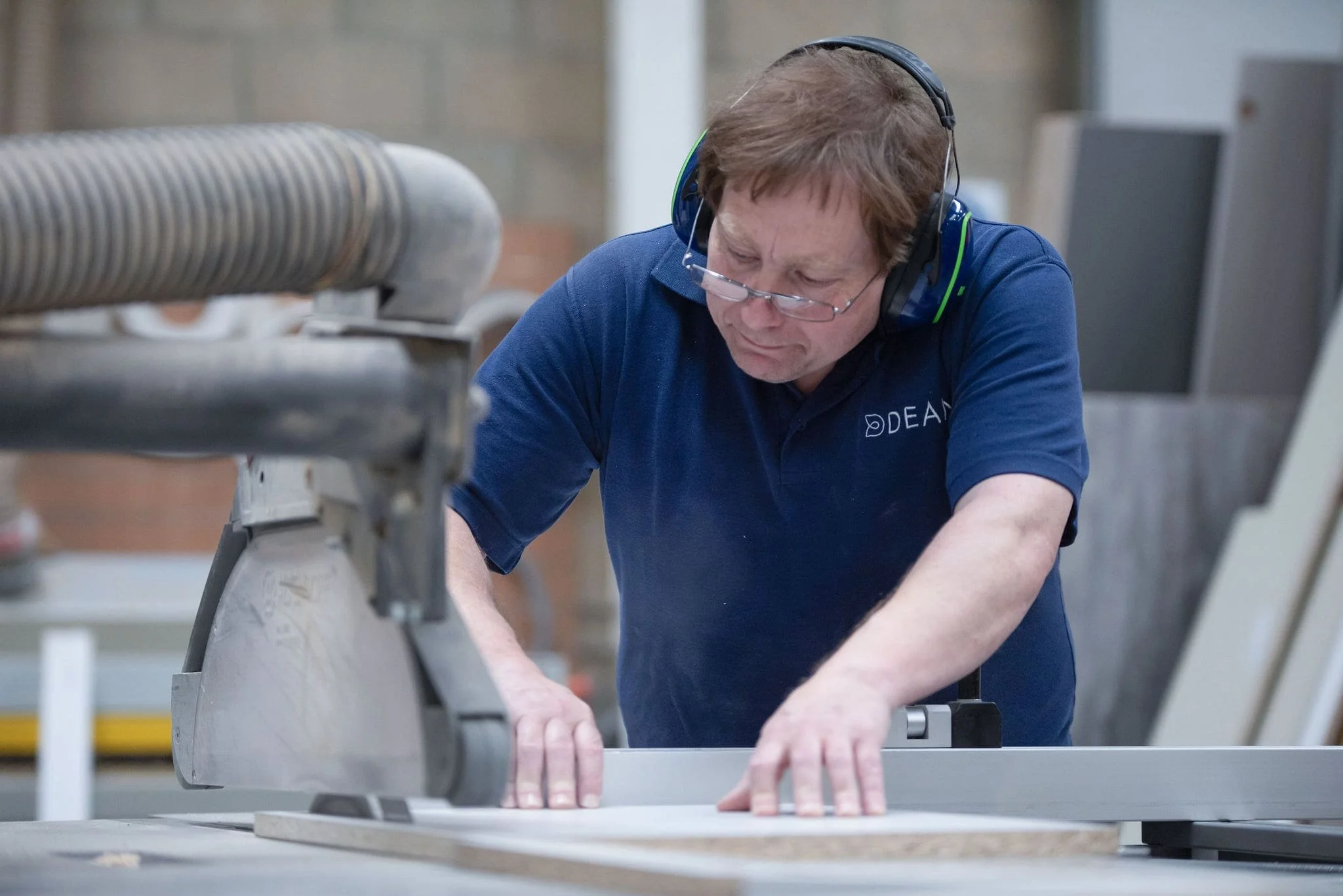 Person operating a table saw with protective gear in a workshop.