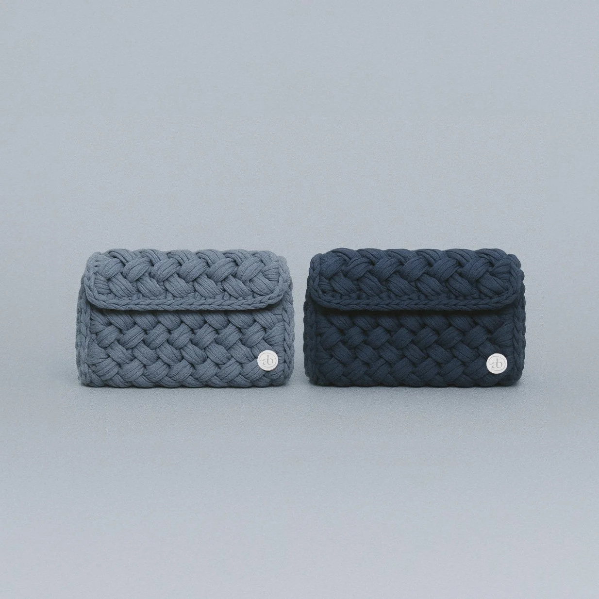 Two woven fabric wallets, one light gray and one dark gray, placed side by side on a plain background.