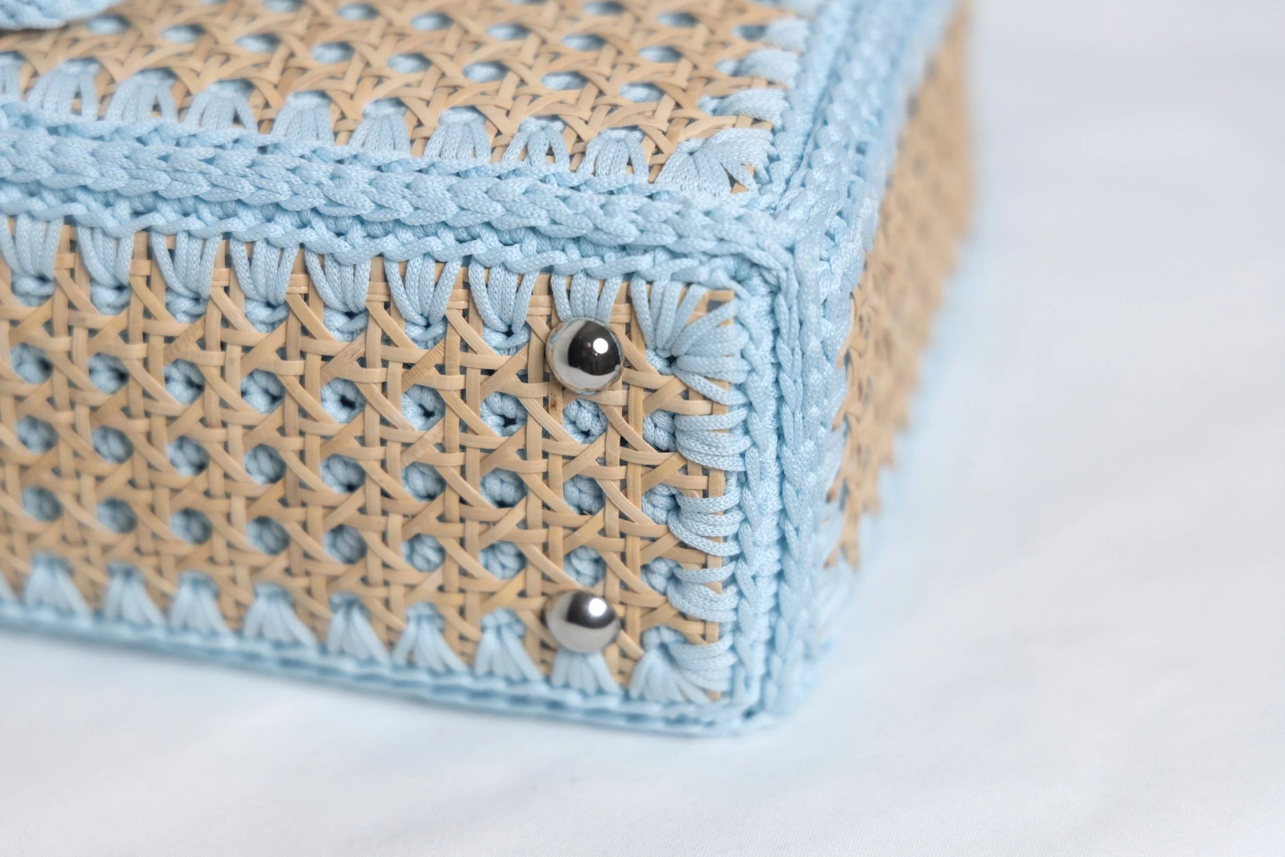 Close-up of a woven wicker box with light blue fabric trim and decorative metal studs.