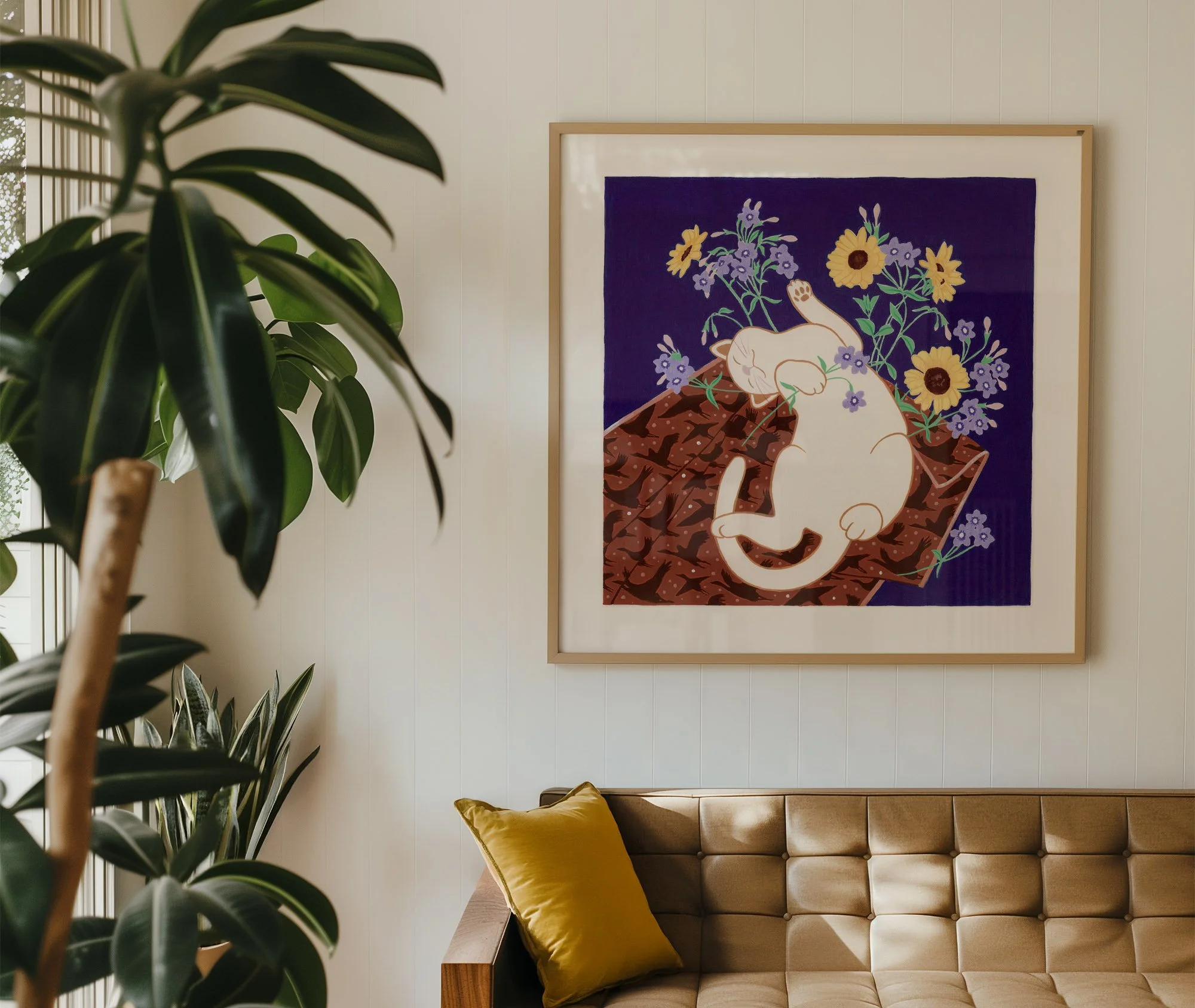 Interior of a living room with a large framed artwork of a sleeping cat surrounded by flowers on the wall, a brown tufted sofa with a yellow pillow, and green houseplants near a window.