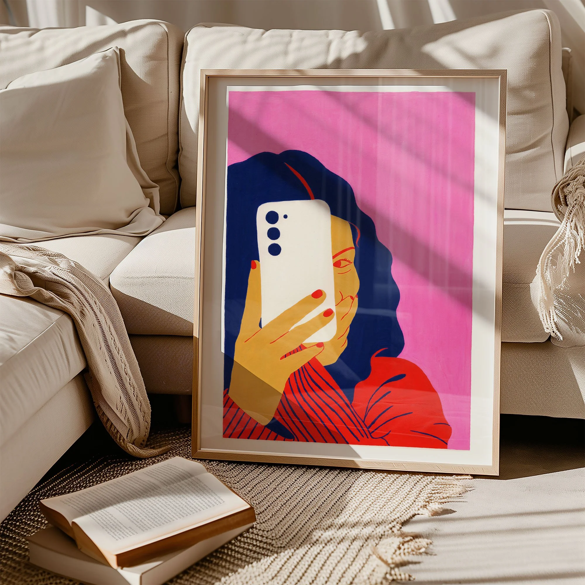 Framed colorful illustration of a woman taking a selfie with a smartphone, sitting on a couch, with sunlight casting shadows on a beige couch and a book on a woven rug.