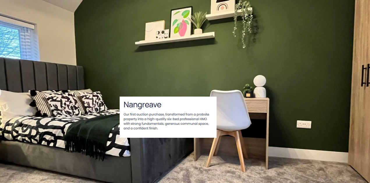 A bedroom with a bed, pillows, and black-and-white bedding, a green feature wall with floating shelves holding frames, artwork, and plants, a small desk with decor, a white chair, and a wooden wardrobe.