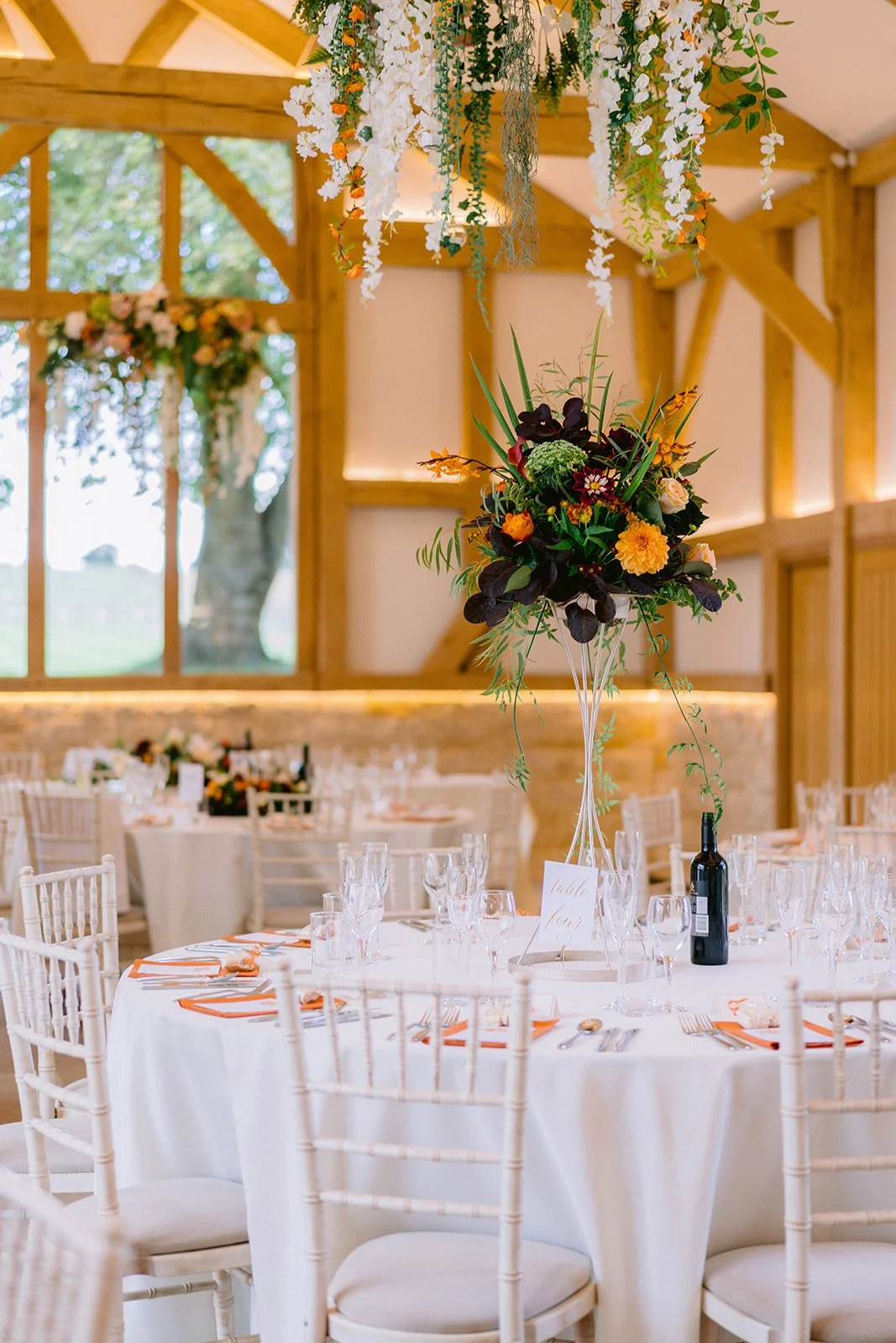 Elegant banquet table set with white tablecloth, glassware, and floral centerpiece in a rustic wooden venue.