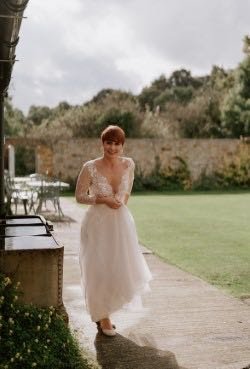 A woman in a wedding dress walking outdoors on a pathway in a garden setting.