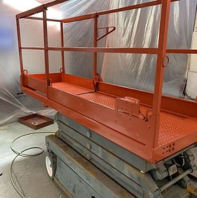 Orange mobile work platform or scaffolding on wheels inside a workshop or construction area.