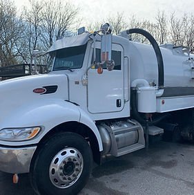 A large white tanker truck parked outdoors with leafless trees in the background.
