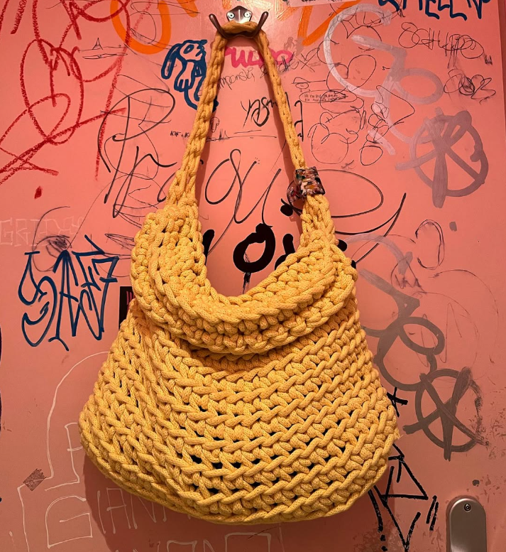 Gelbe, handgeknüpfte Tasche an einer graffiti-verzierten Wand.
