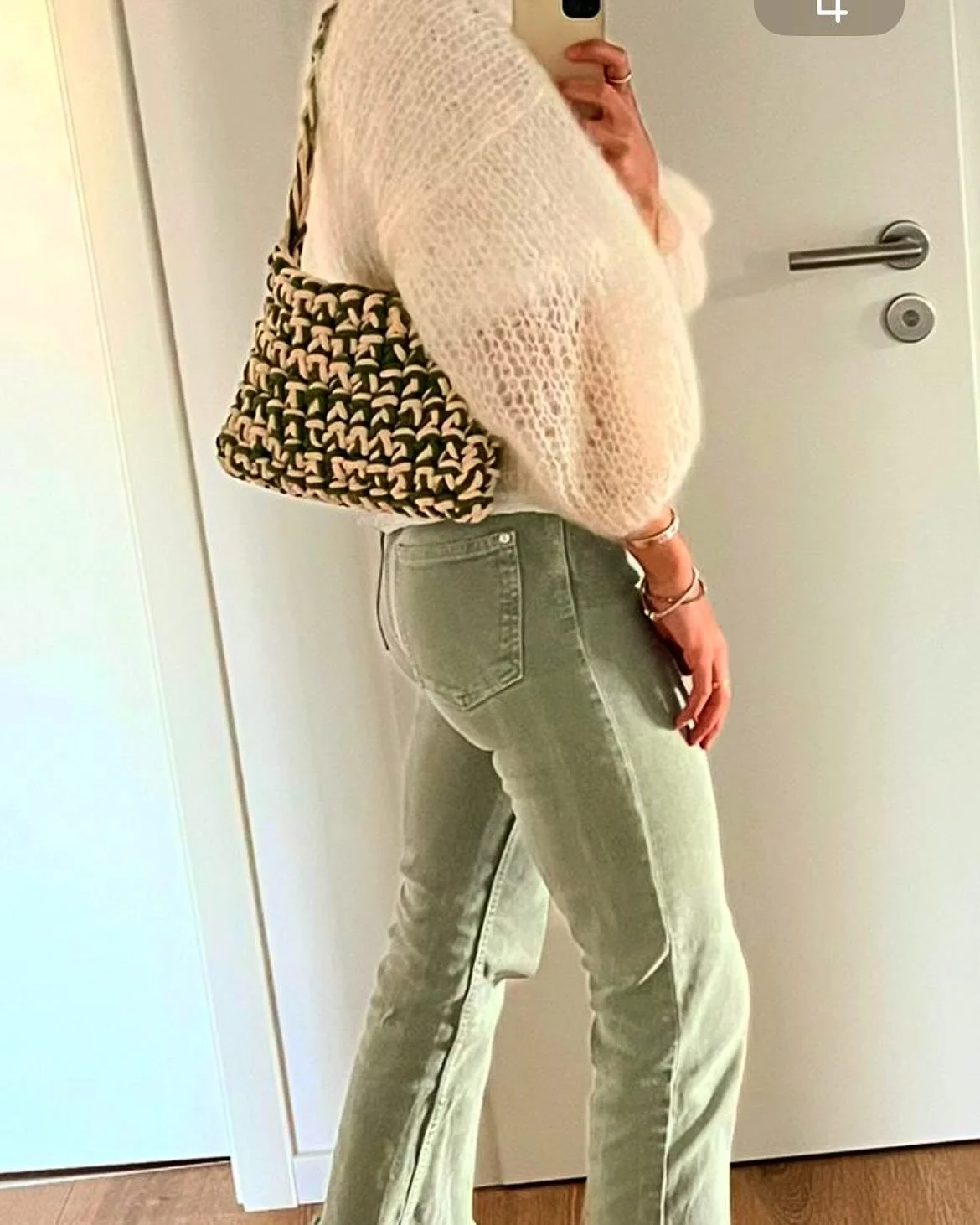 Frau in gelben Jeans, cremefarbenem Pullover und einer Handtasche macht ein Selbstporträt im Spiegel.