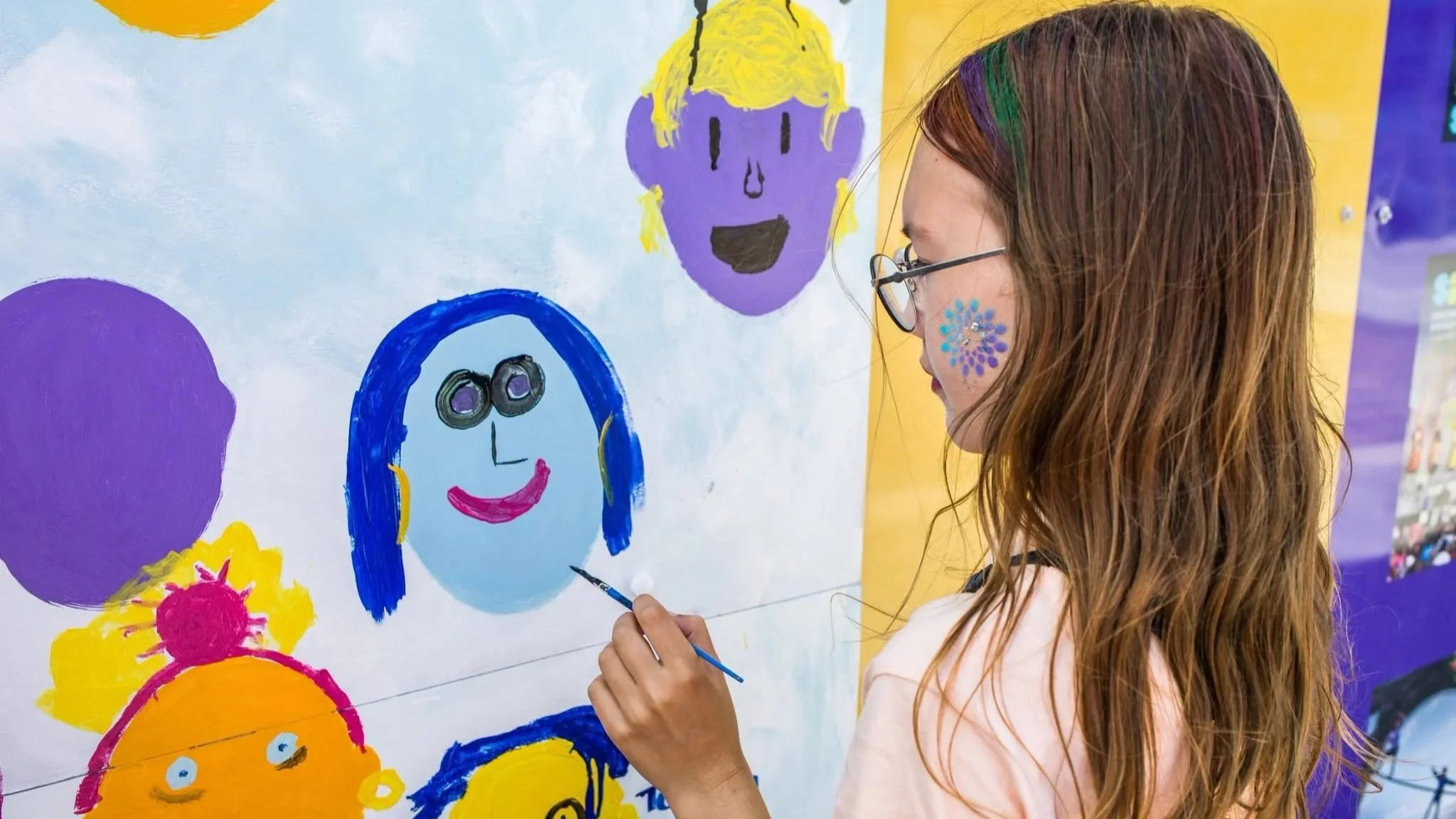 A young girl paints a colourful face, adding to the community art wall.