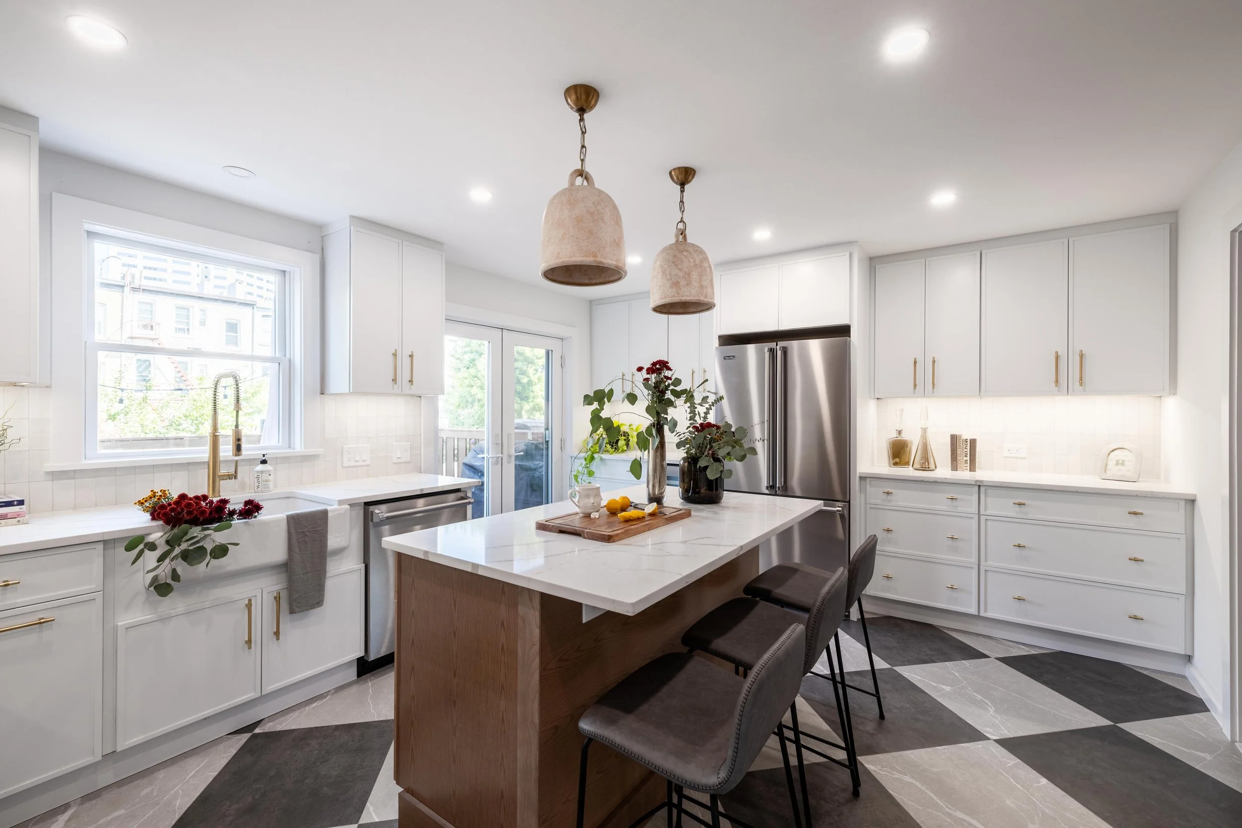 Modern kitchen with white cabinets, stainless steel appliances, center island, pendant lights, and decorative plants.