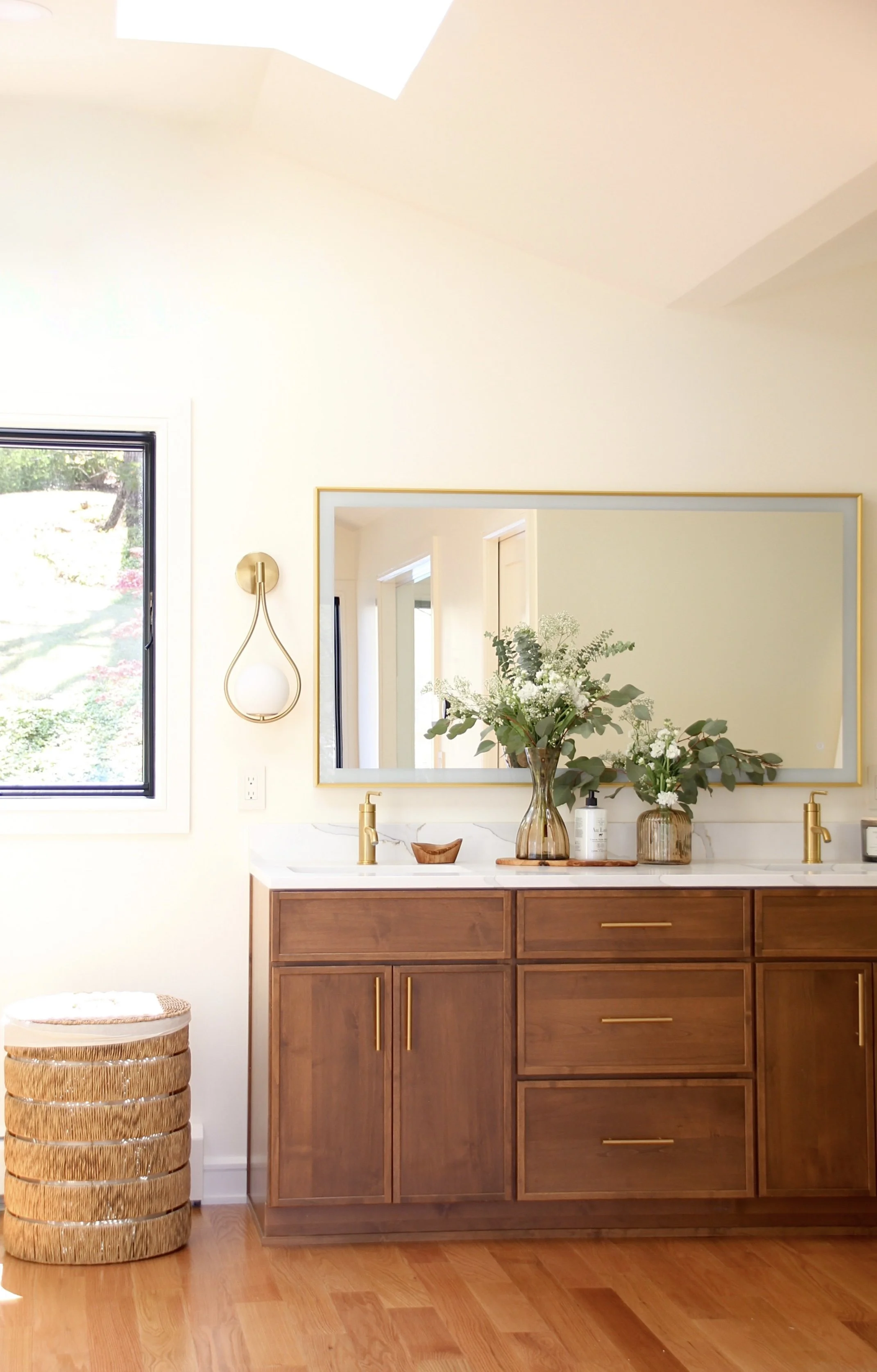 Luxurious bathroom with wooden vanity, gold faucets, large mirror, and decorative plants.