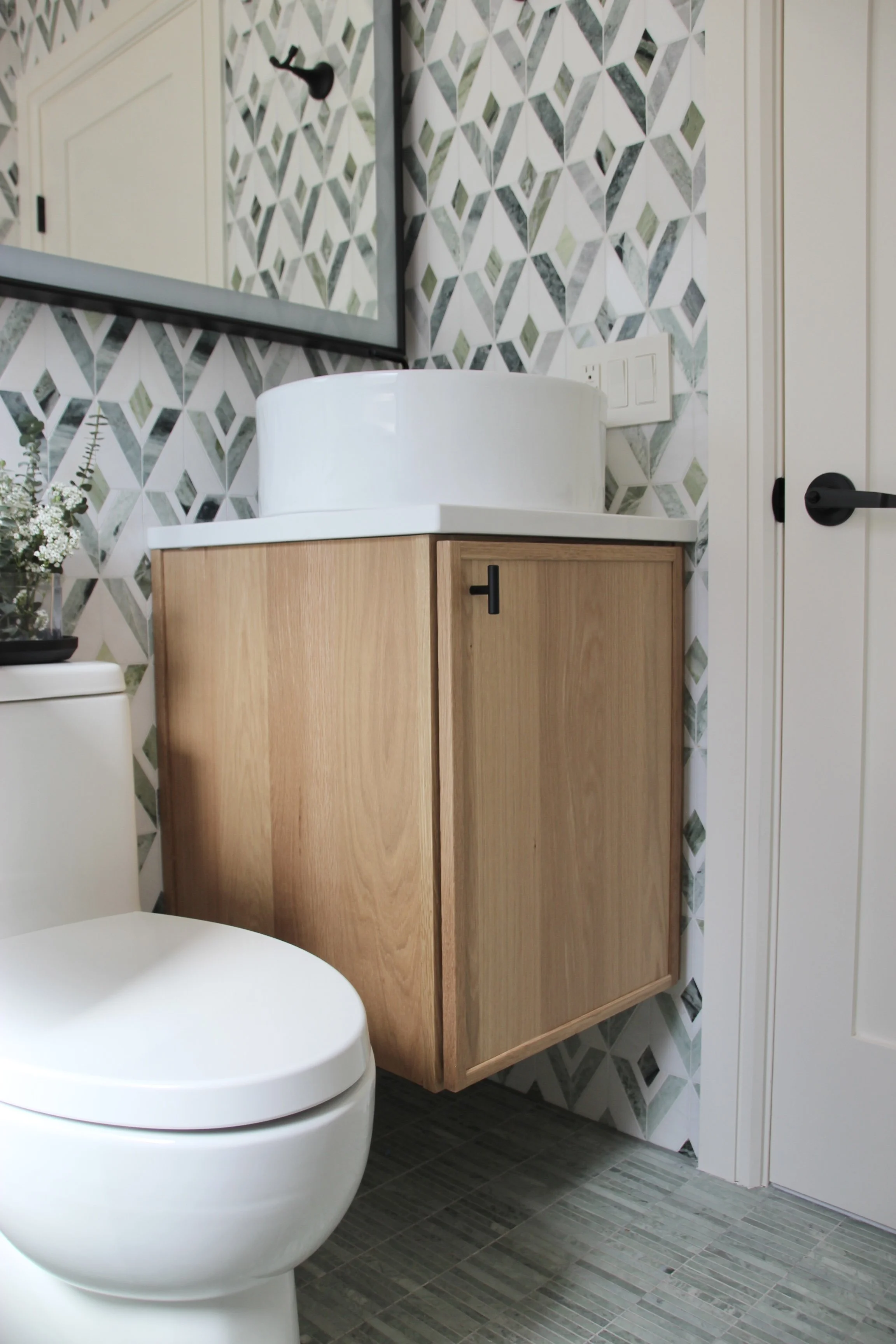 Modern bathroom with a round white sink on a wooden vanity, geometric patterned wallpaper, and a white toilet.