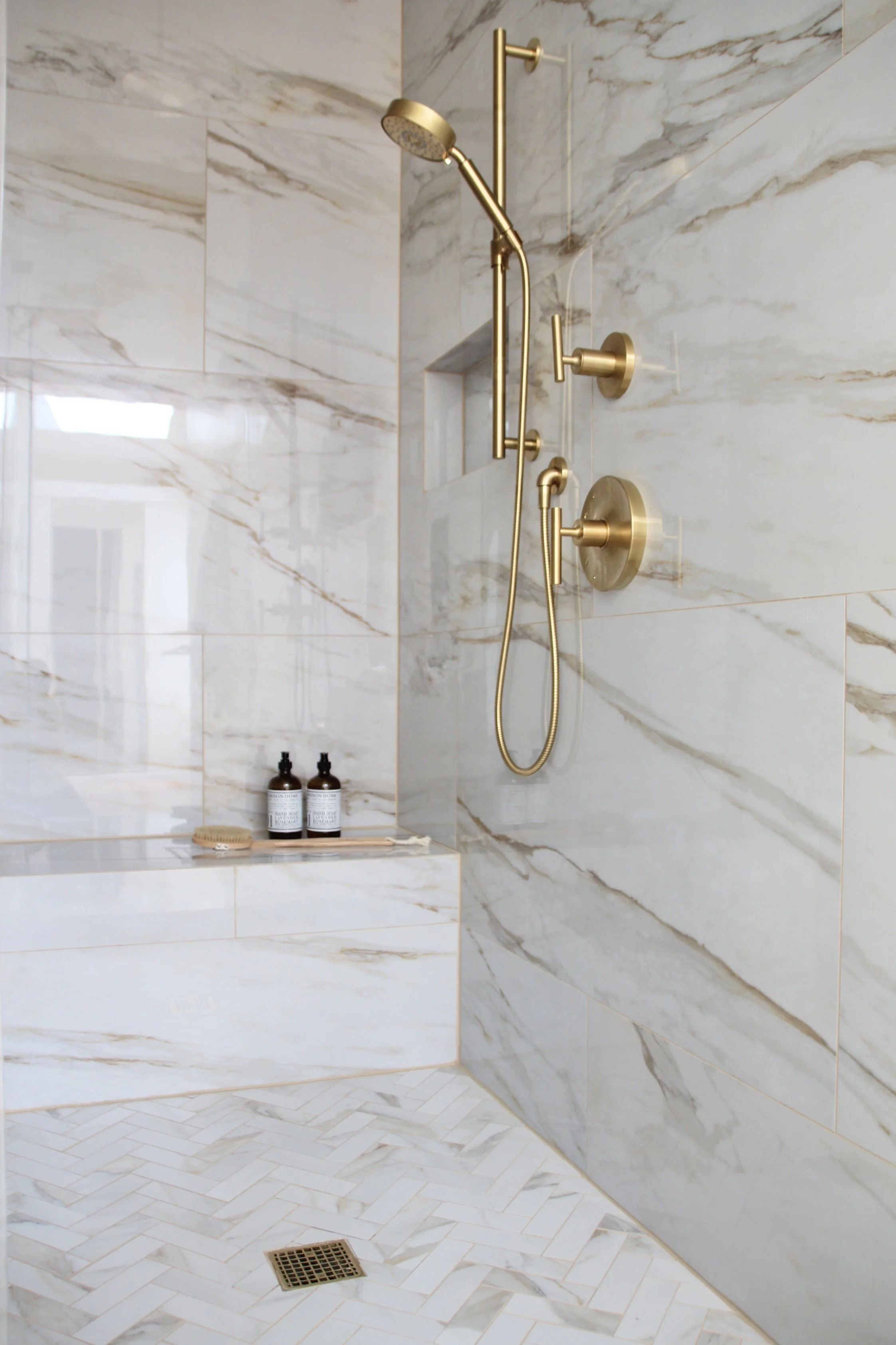 Luxury marble shower with gold fixtures and herringbone floor tiles.