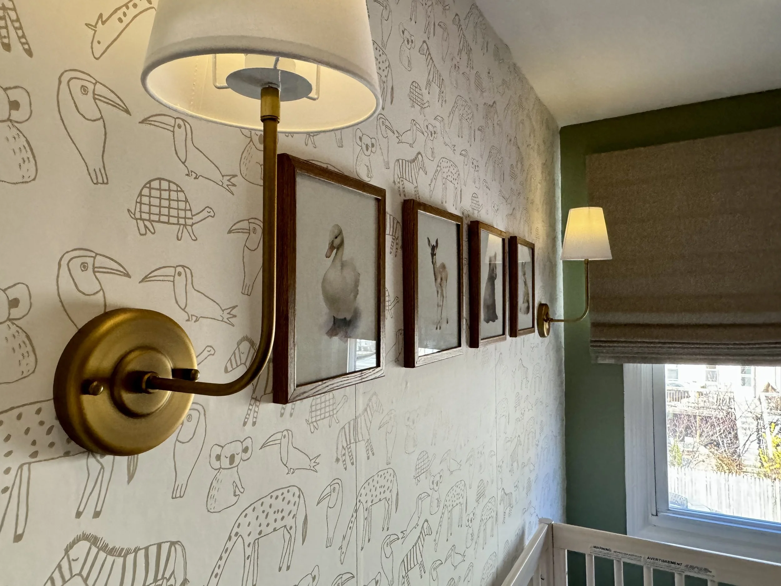 Nursery with animal wallpaper, framed animal photos, wall-mounted lamps, crib, and window with blinds.