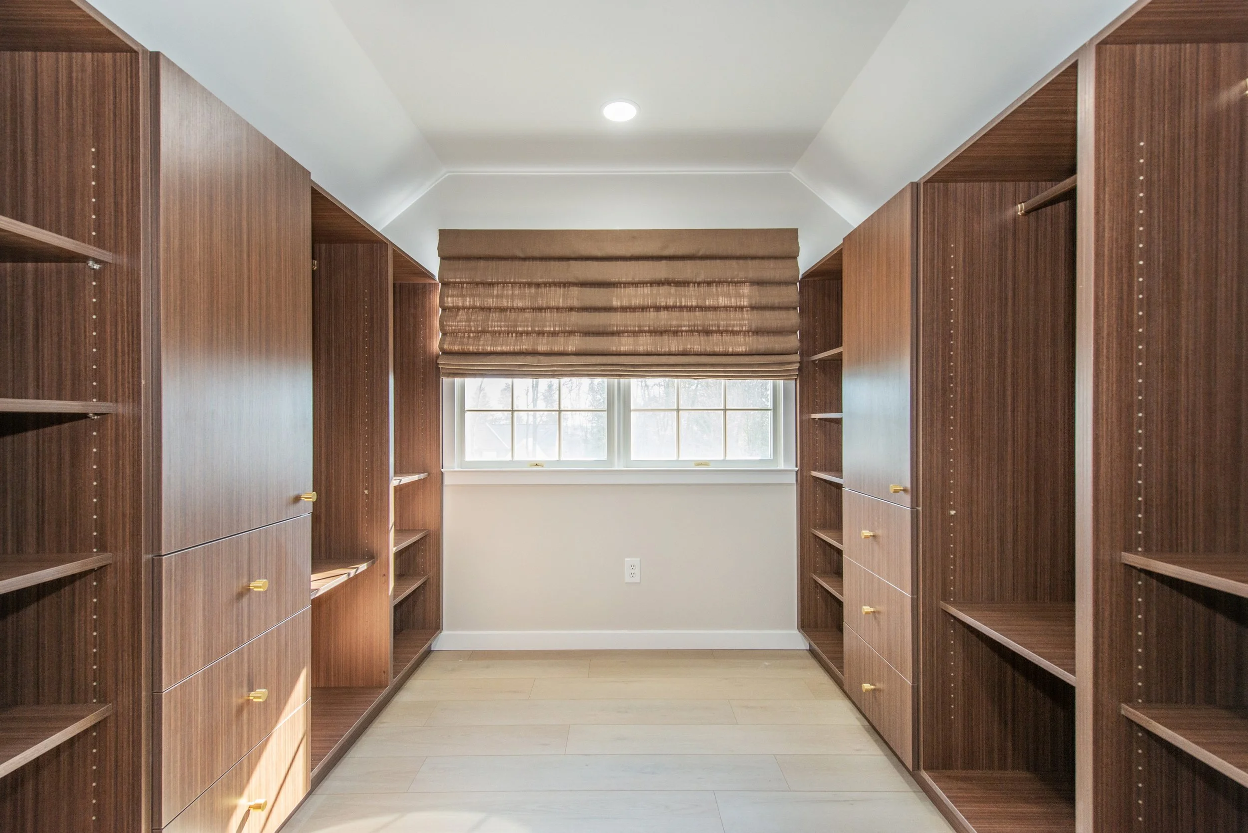 Walk-in closet with wooden shelves and drawers, window with blinds