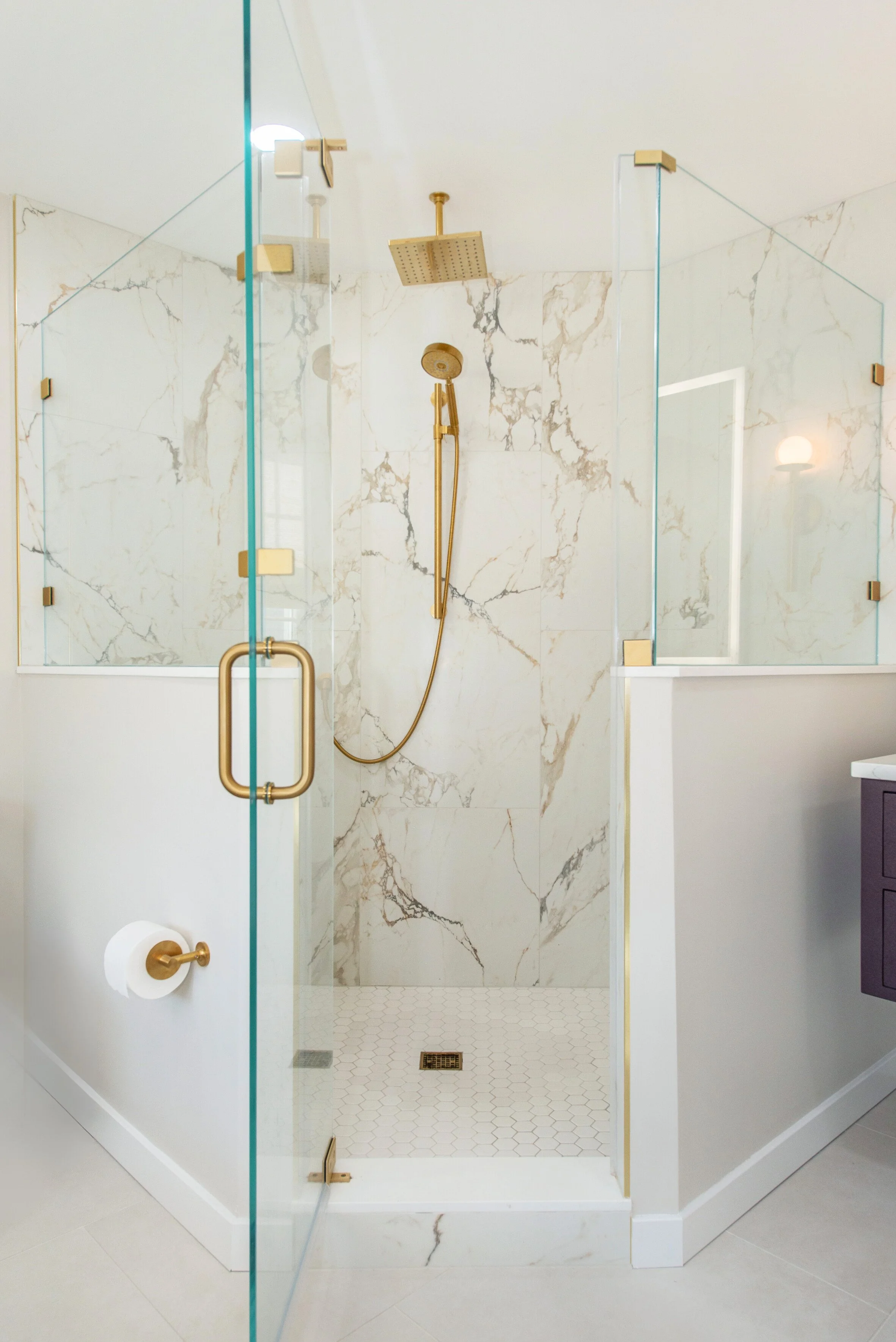 Modern shower with glass doors, gold fixtures, and marble walls